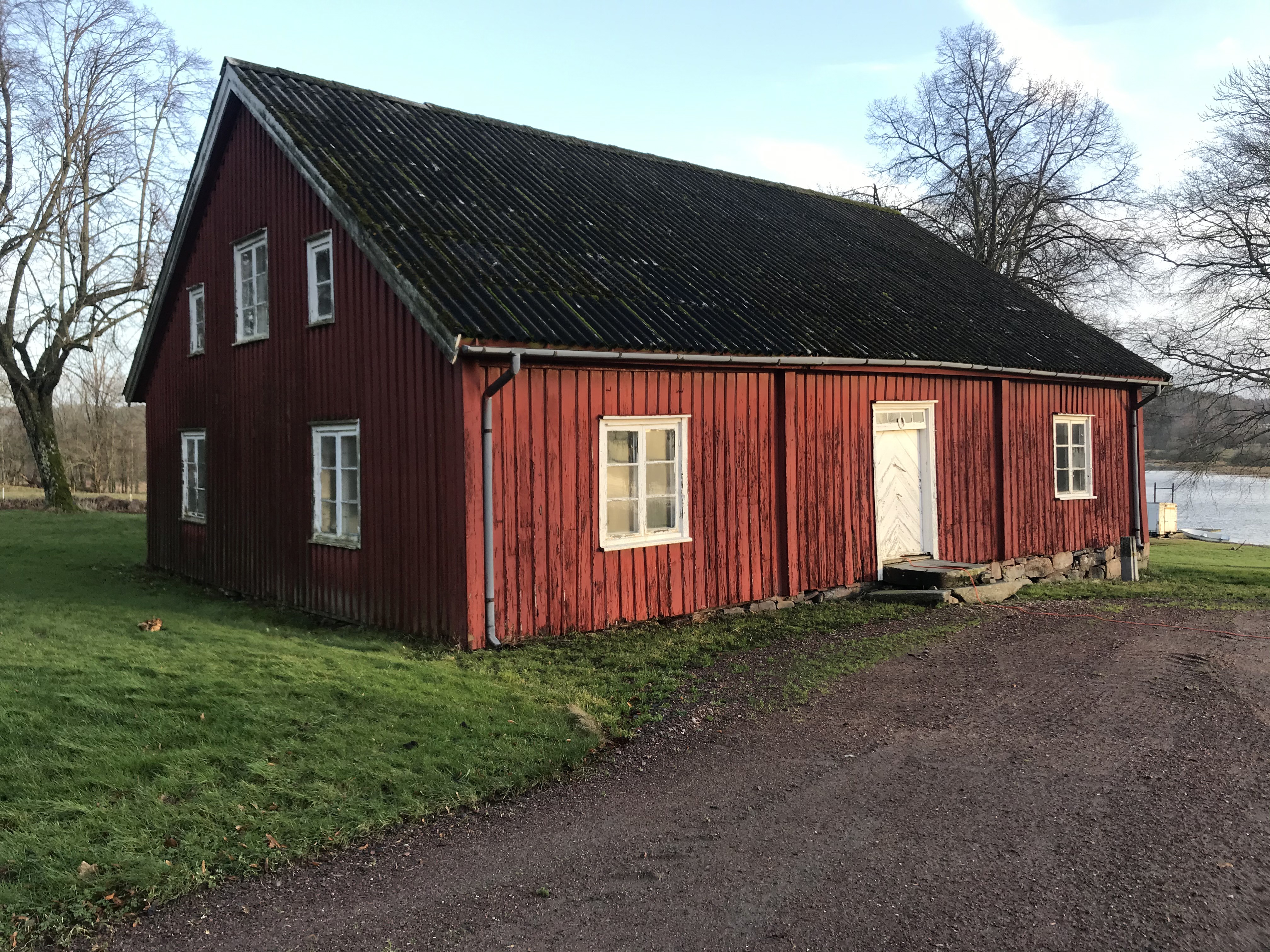 Kastellegården. Flygelbyggnad i rödmålat trä med vita snickerier runt dörr och fönster. I bakgrunden skymtar Nordre älv.