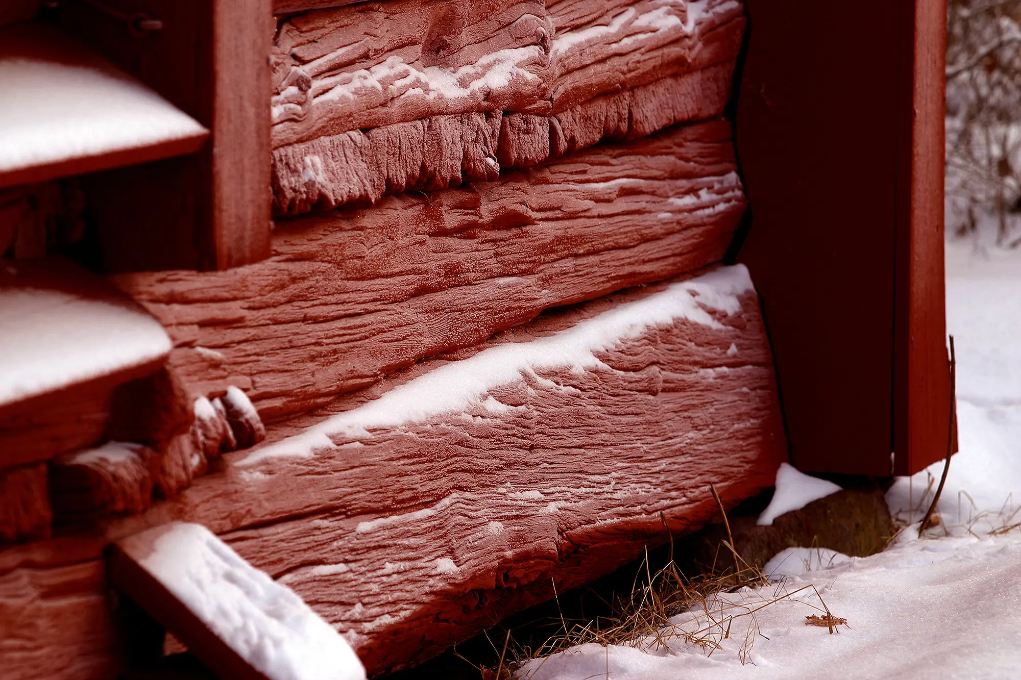 En faluröd träfasad i närbild. På marken ligger snö.