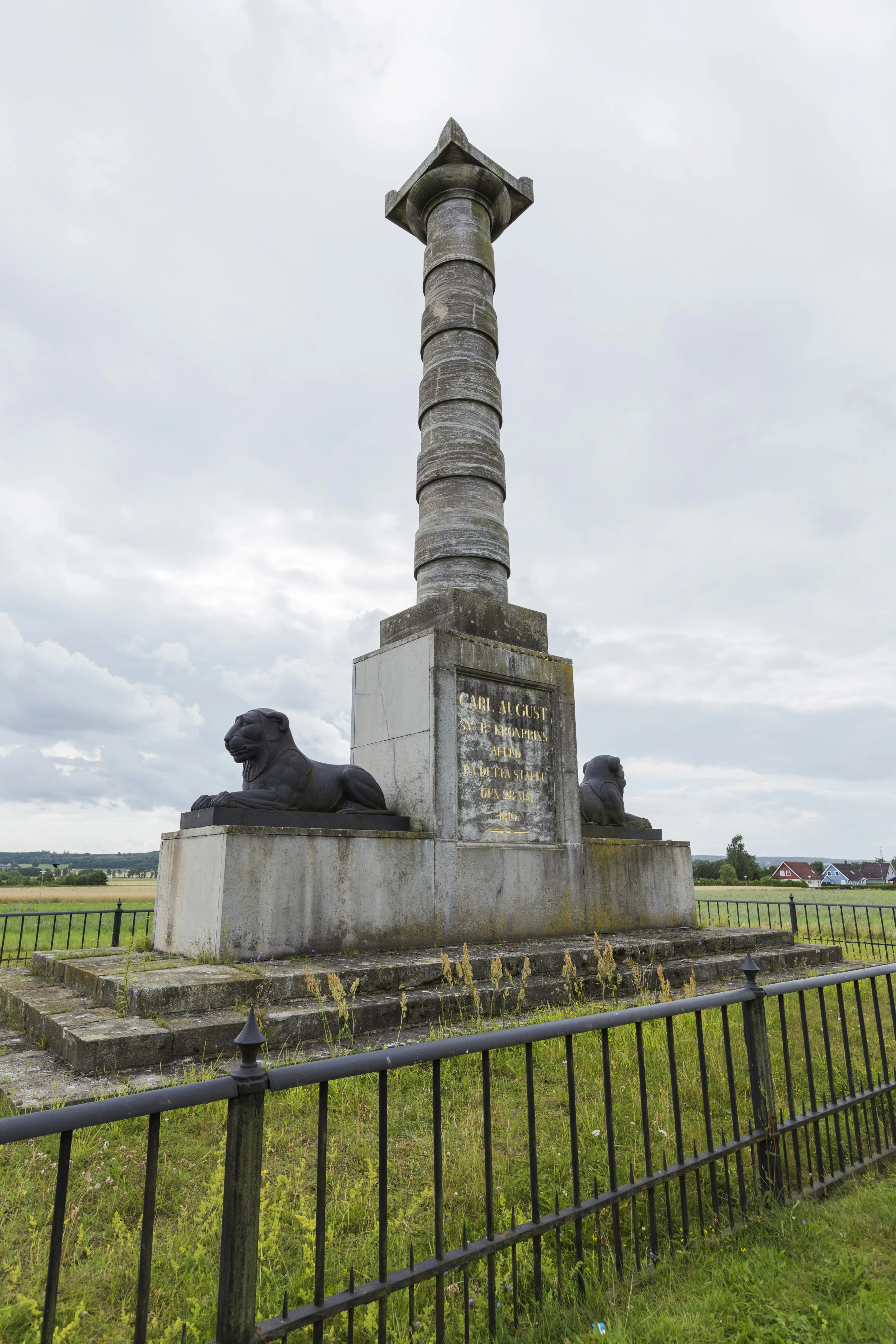Kvidingemonumentet. En stenpelare med förgylld inskription, flankerad av två lejonskulpturer.