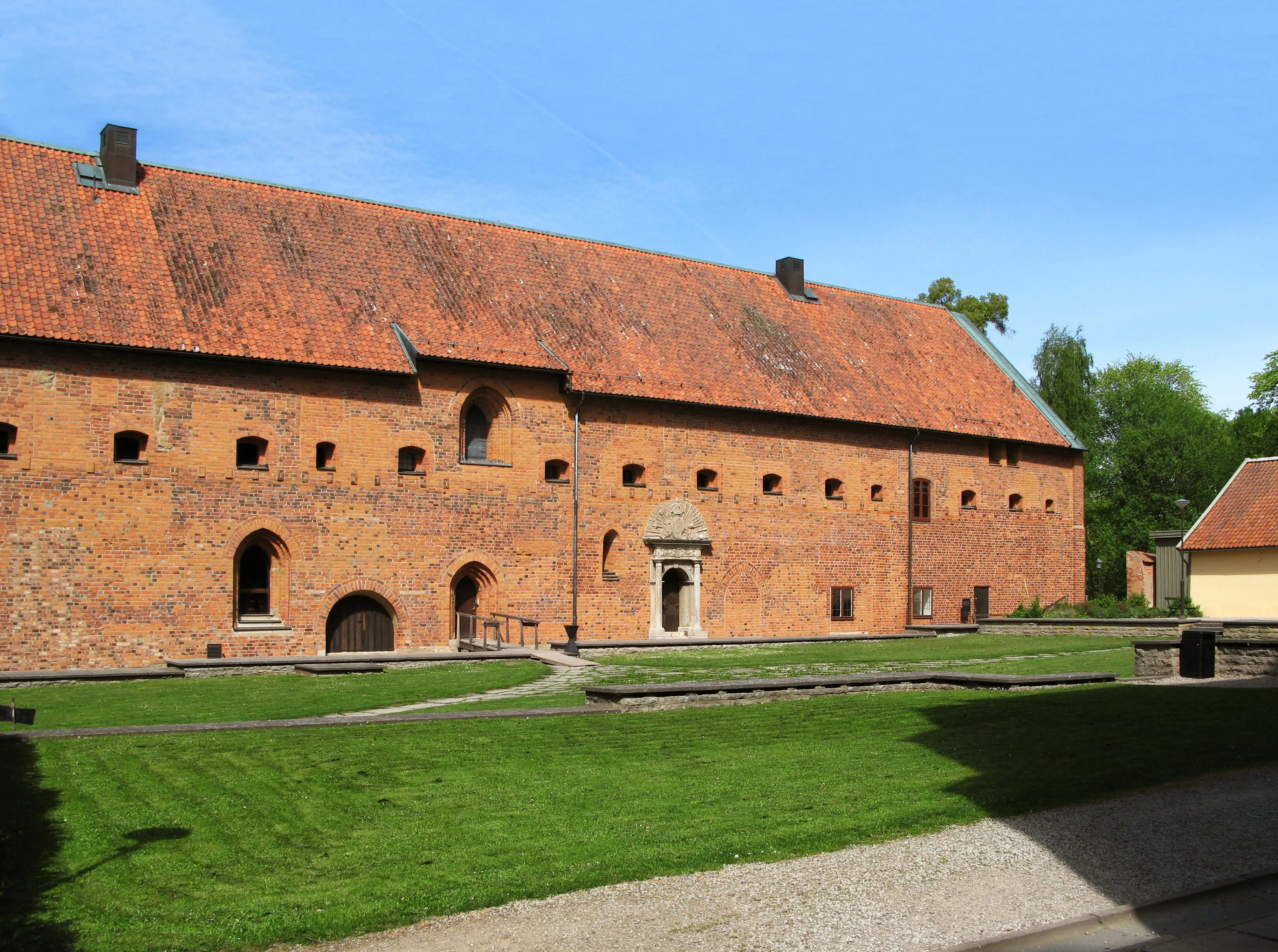 Tegelbyggnad med tegeltak med grön gräsplan framför.