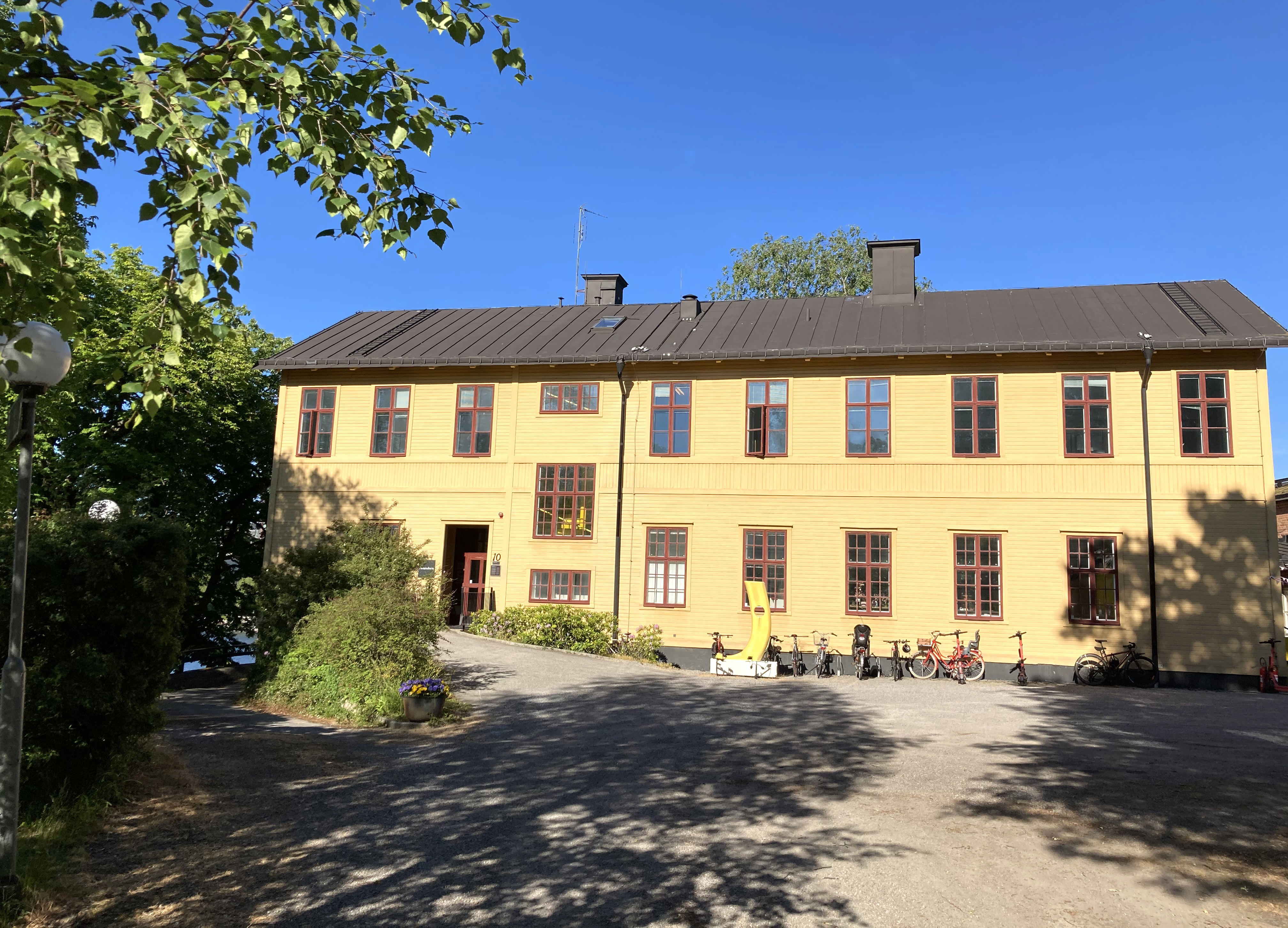 Sjöreservens kasern, Skeppsholmen. En tvåvåningsbyggnad klädd i gulmålat trä. Sommar och grönska.