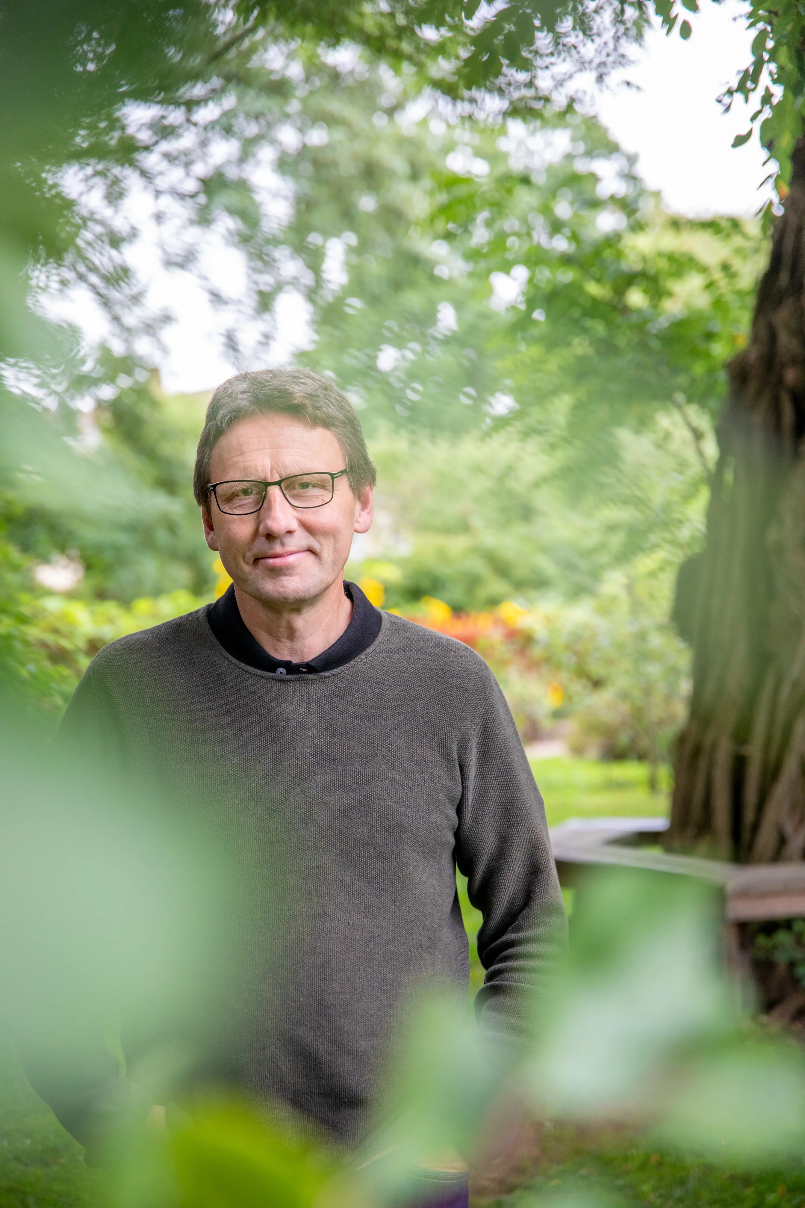 Leende man med glasögon bakom grönska.