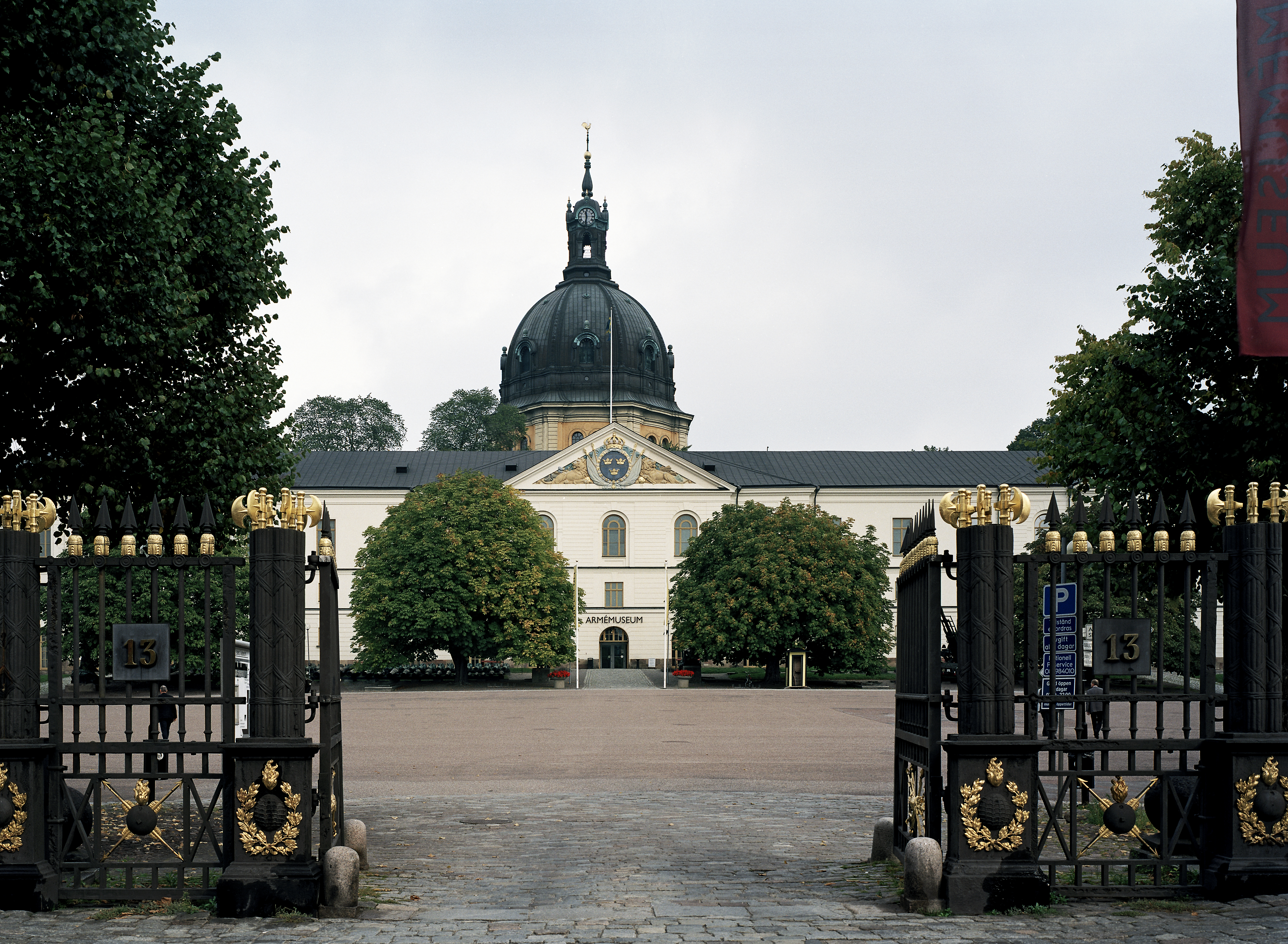 Ingången till Artillerigården går genom grindar i ett ståtligt gjutjärns-staket med förgyllda detaljer. Byggnaderna omger en stor gårdsplan.