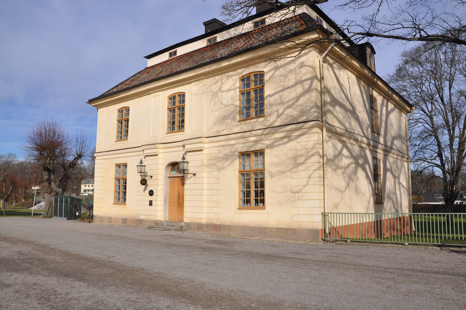Hus med säteritak. Fasaden är i ljus puts. Dörr och och fönsterstommar är målade i en orange eller brun kulör.