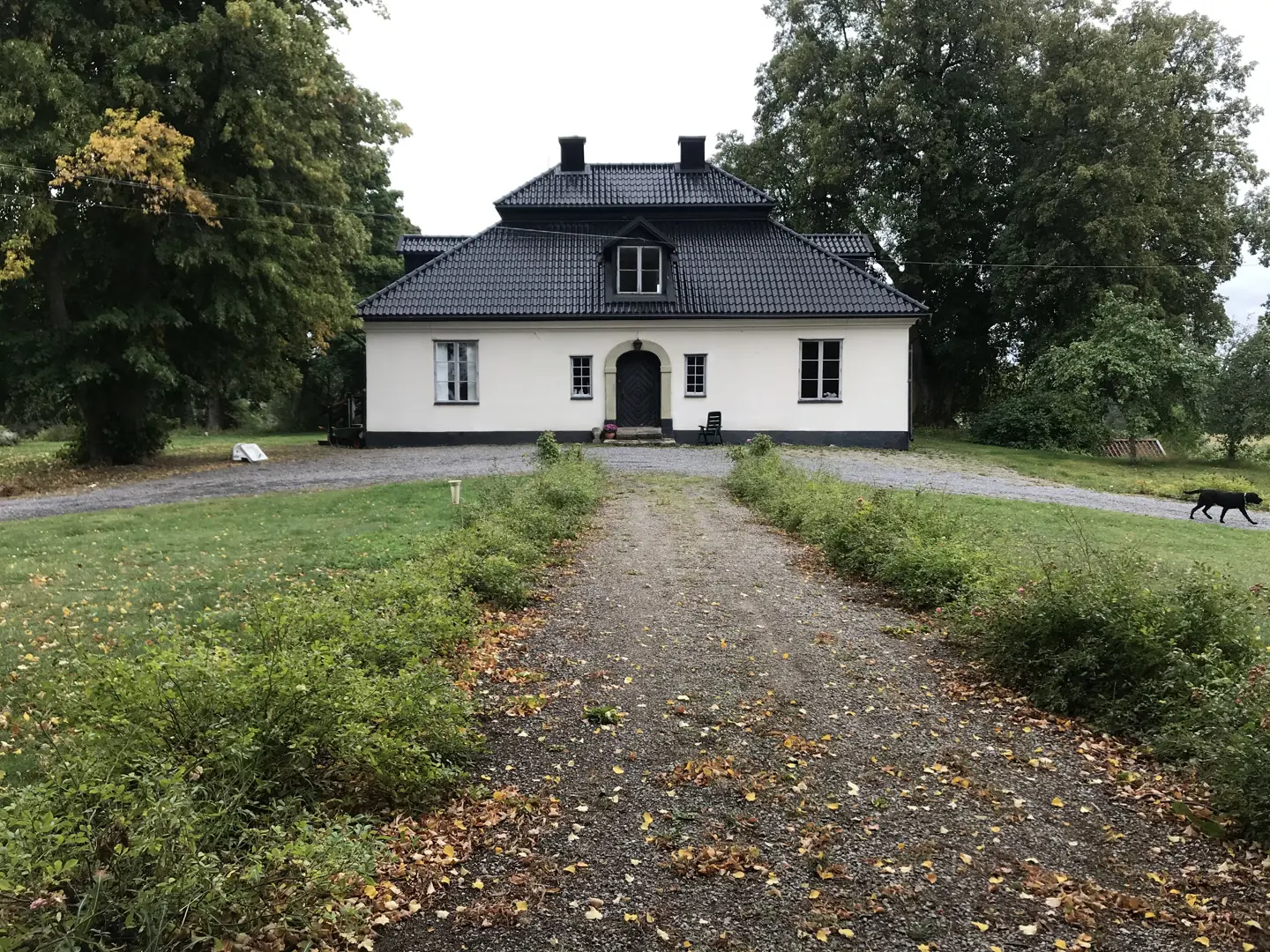 En byggnad med vitputsad fasad och svart tak tagen från en grusgång.