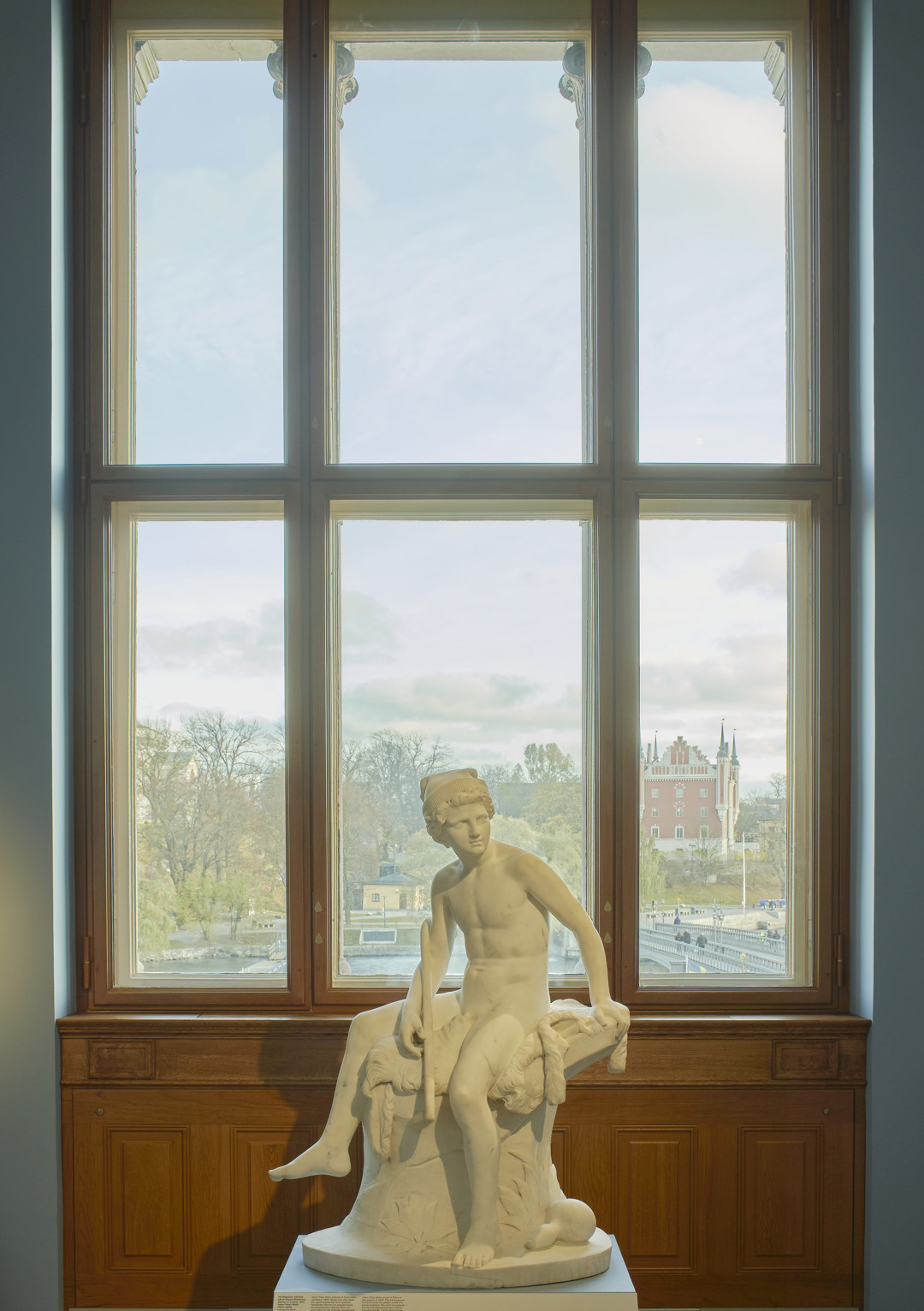 Skulptur framför ett fönster med utsikt mot Skeppsholmen och Amiralitetshuset.