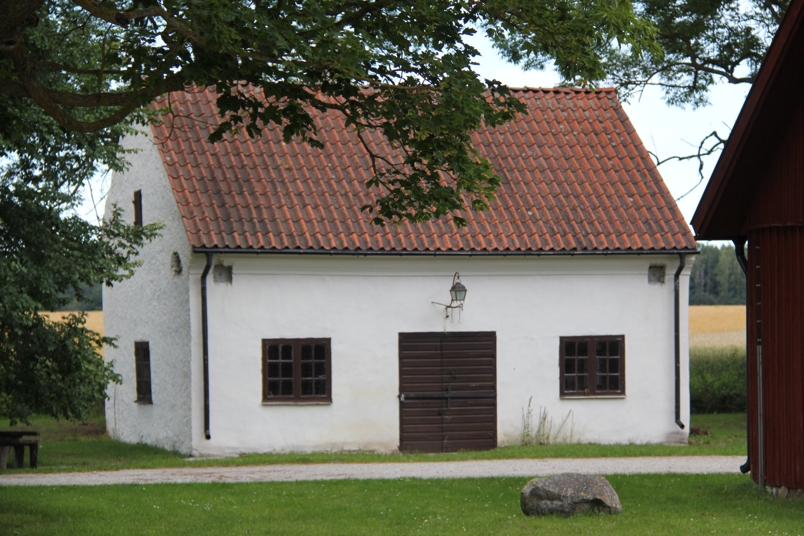 Roma kungsgård. Liten, vitputsad byggnad med tegeltak, spröjsade fönster och en bred port. Ovanför porten sitter en lykta.