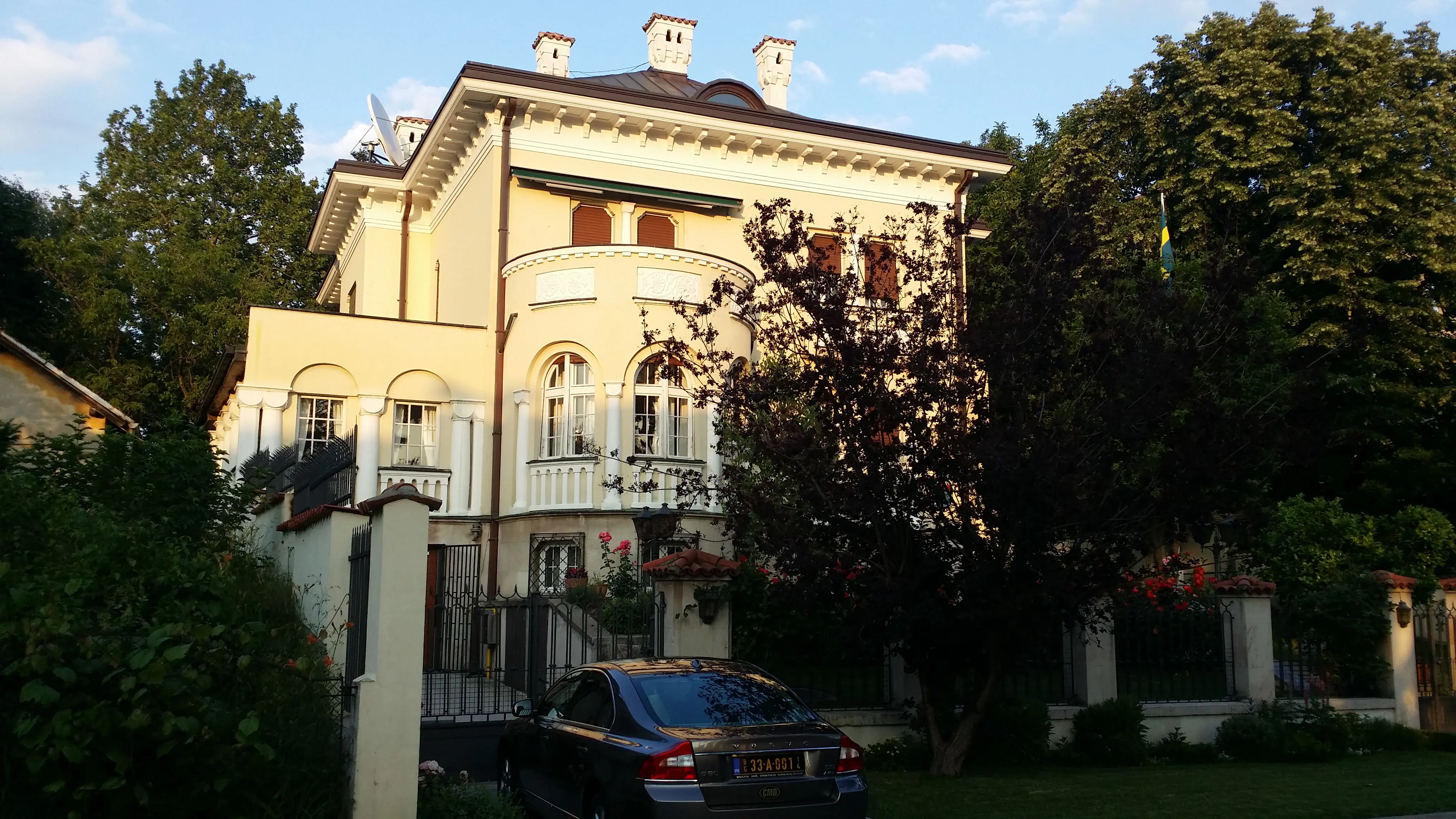 Ambassaden i Belgrad. En klassicistisk villa i gräddvit puts, inramad av lummig växtlighet. Ett högt smides-staket omger huset.