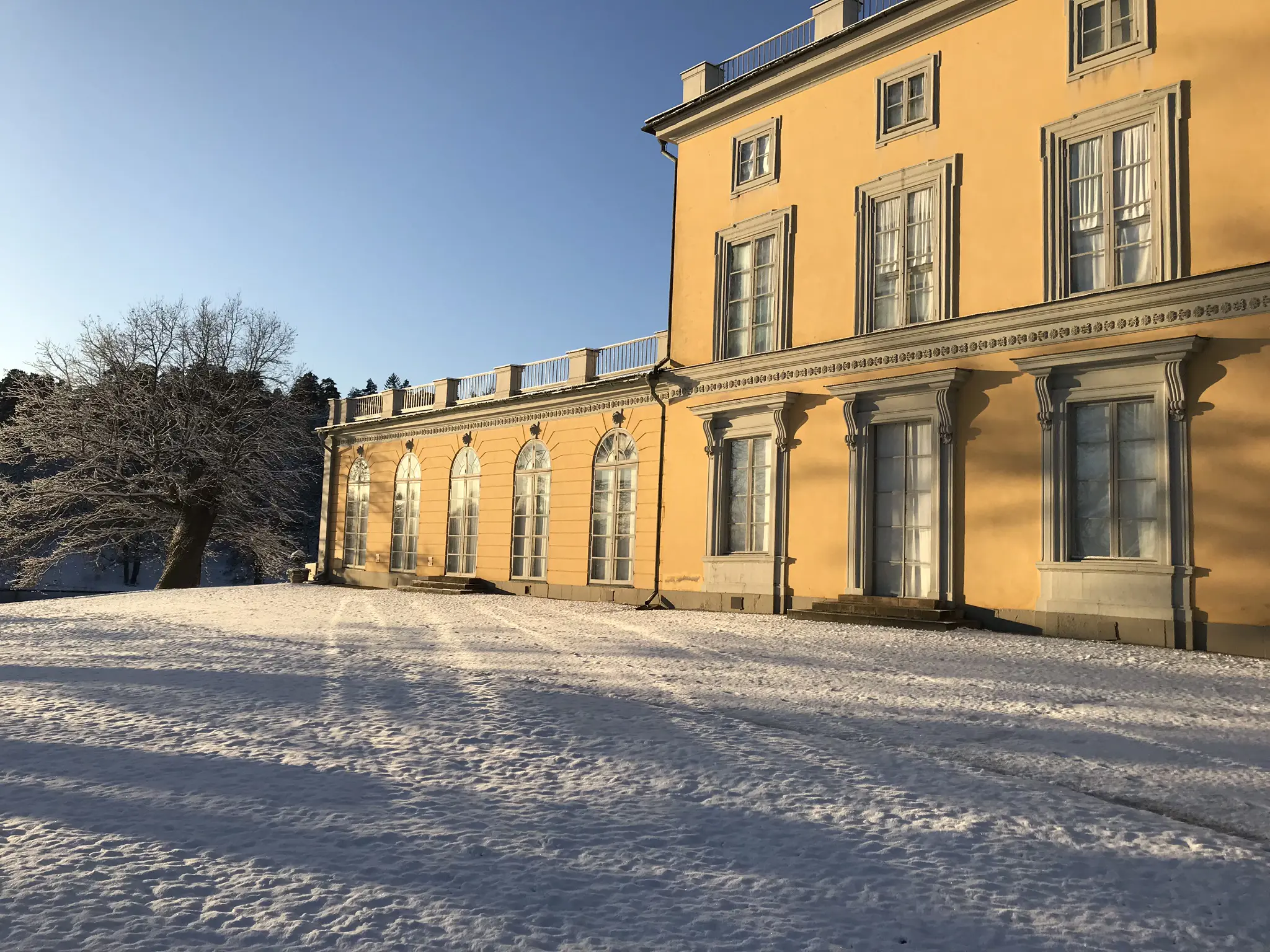 Gustav III:s paviljong i Hagaparken. Ett gult litet slott. Mittdelen har tre våningar och flyglarna en våning. Vinter och snö.