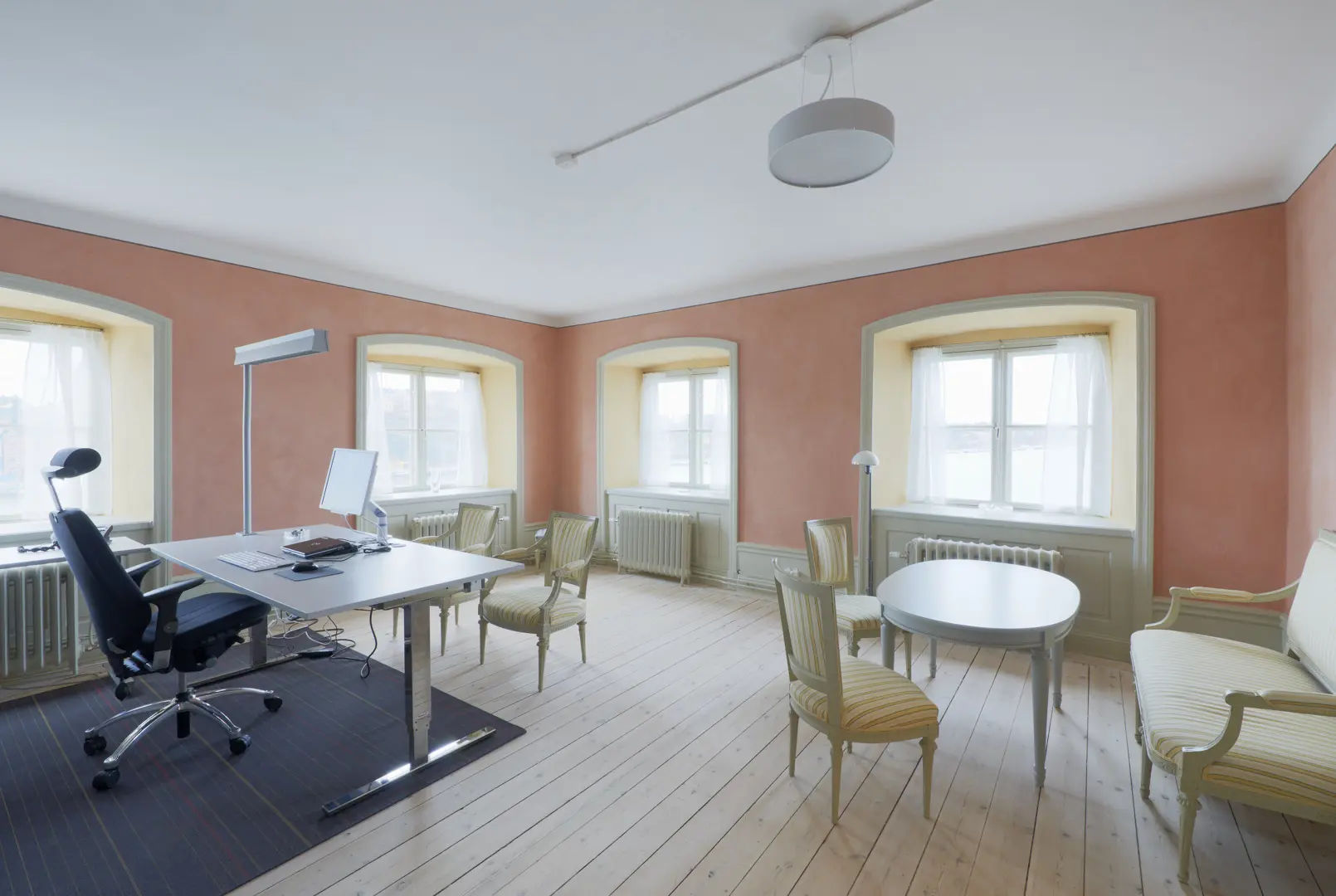 Rum med en modern kontorsplats och ett i övrigt klassiskt möblemang med gröna fåtöljer och en soffa. Väggarna är rosaaktiga.