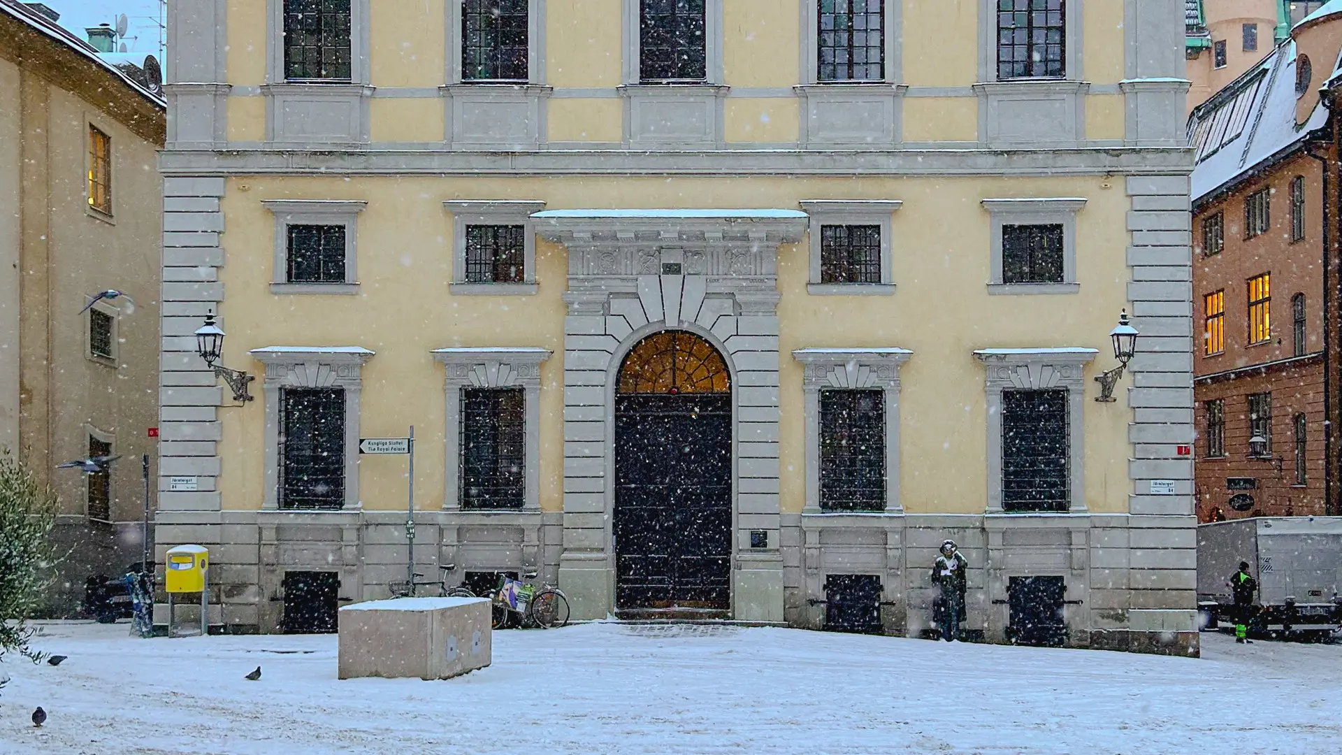 Södra Bankohusets fasad mot Järntorget. En ljusgul byggnad med stensockel och stor stenportal. Snö faller ymnigt.