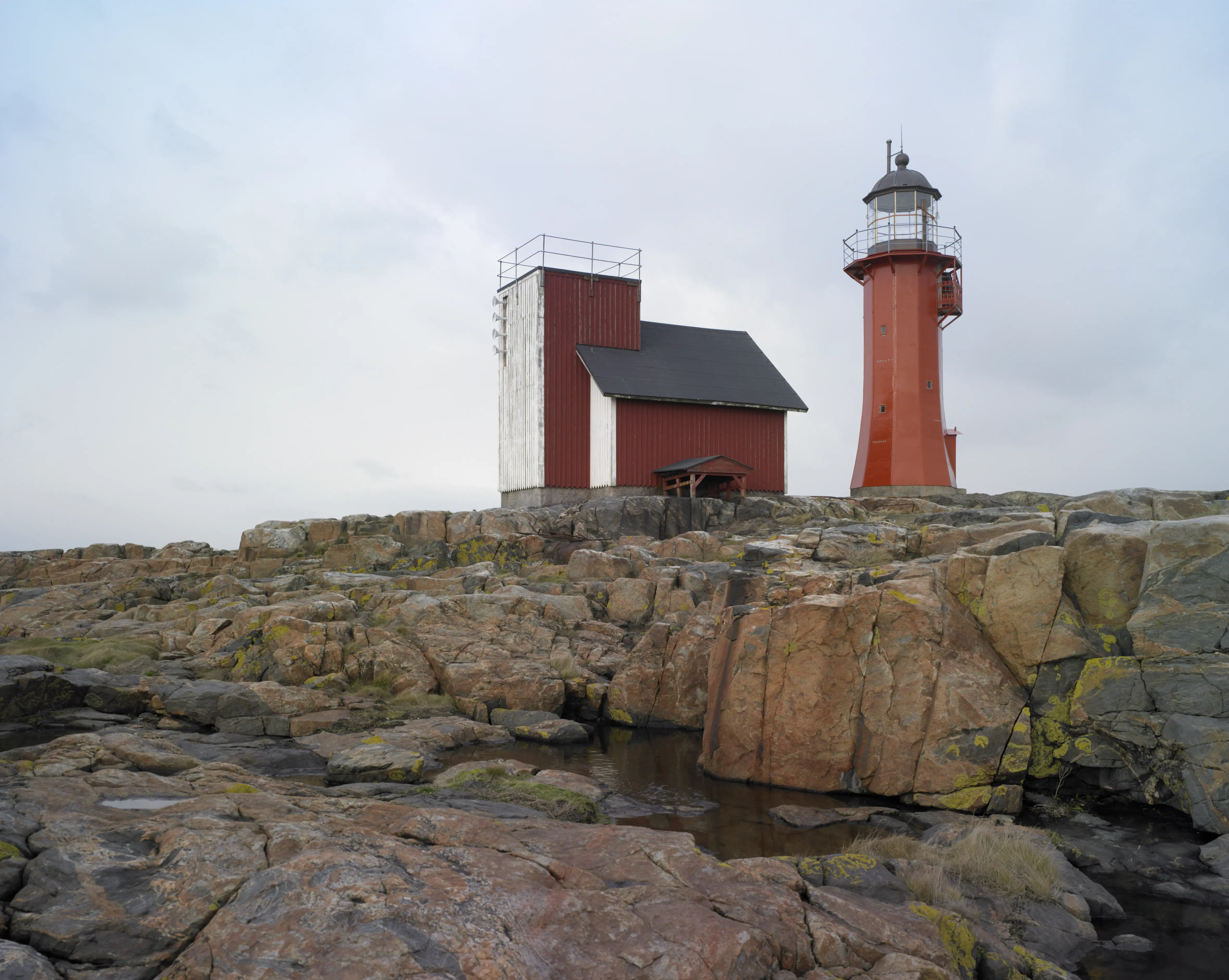 Tylöns fyr, klädd i rödmålad plåt. Intill ligger en träbyggnad målad i rött och vitt.