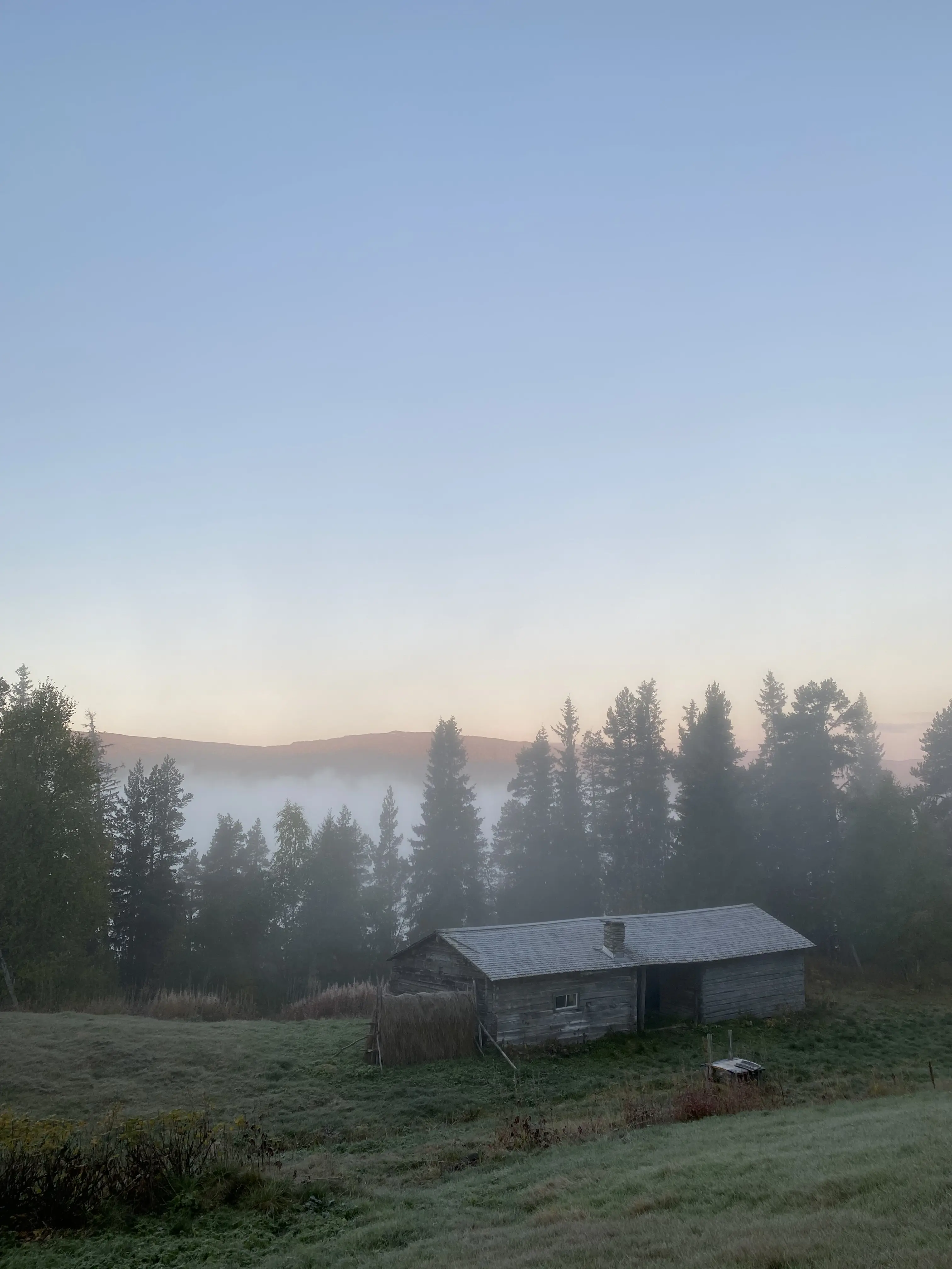Fjällsluttning med grått trähus. I bakgrunden syns en dal fylld med dimma.