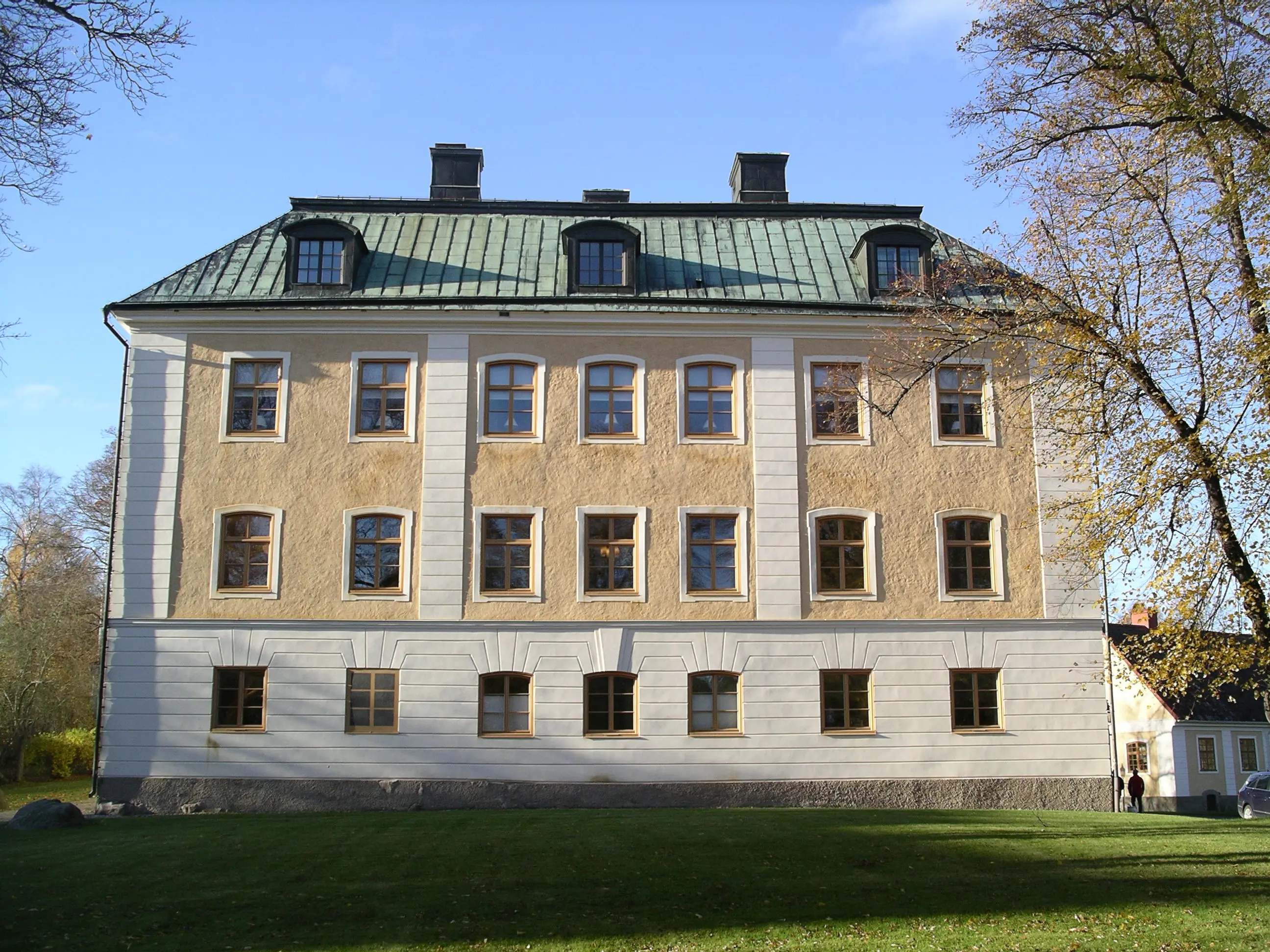 En ljusgul putsad fasad med tre rader av fönster och ett grönärgat koppartak.