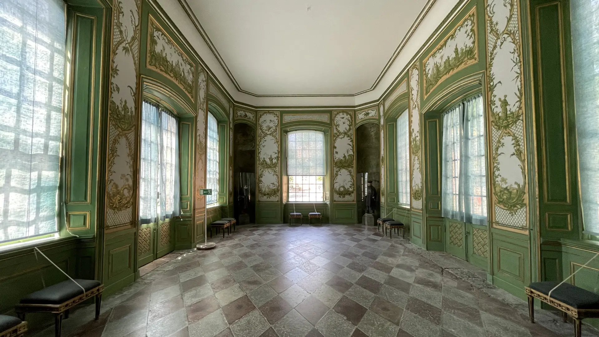 Sal i Kina slott med dagsljus genom tunna gardiner i stora fönster. Väggarna är gröna och vita med målade växtmotiv.