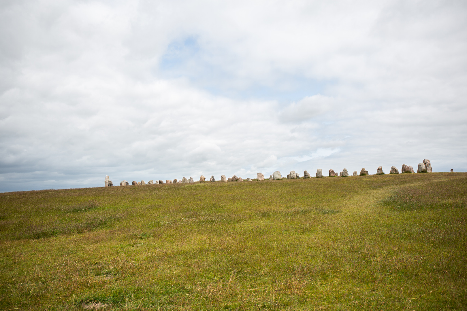 Ales stenar sedda på håll i sin fulla längd. Stenarna liknar en tandad kant på gräs-sluttningen.