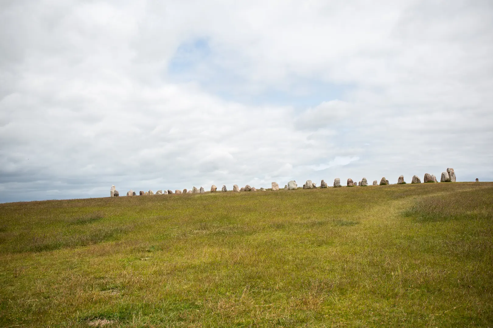 Ales stenar sedda på håll i sin fulla längd. Stenarna liknar en tandad kant på gräs-sluttningen.