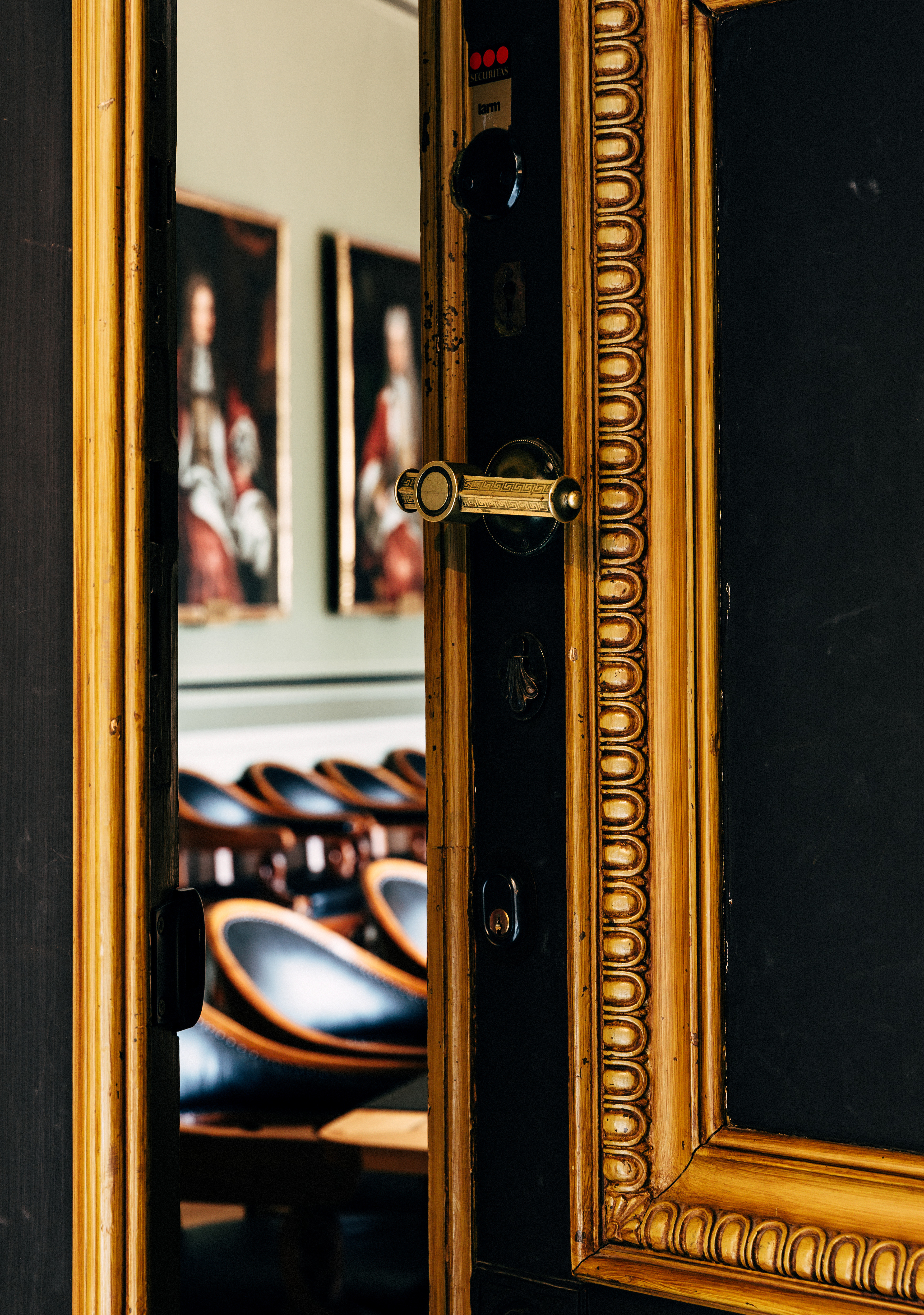 Universitetshuset i Lund. En svart dörr med förgyllda, snidade lister står på glänt. Innanför skymtar ett konferensrum med tavlor och skinnstolar.