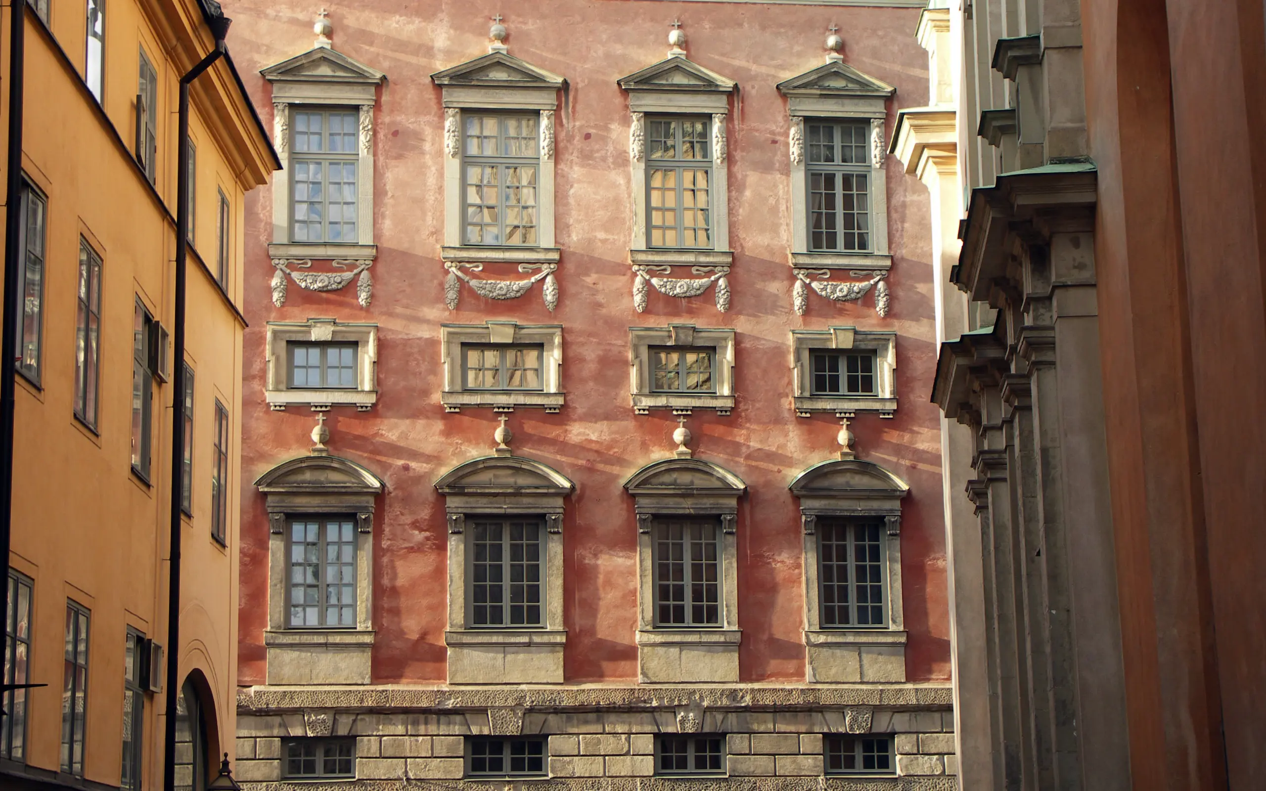 Oxenstiernska palatset sett från gränden Trångsund. Fasaden är rödputsad och de olika utformade fönstren är inramade av klassicistisk stendekor.