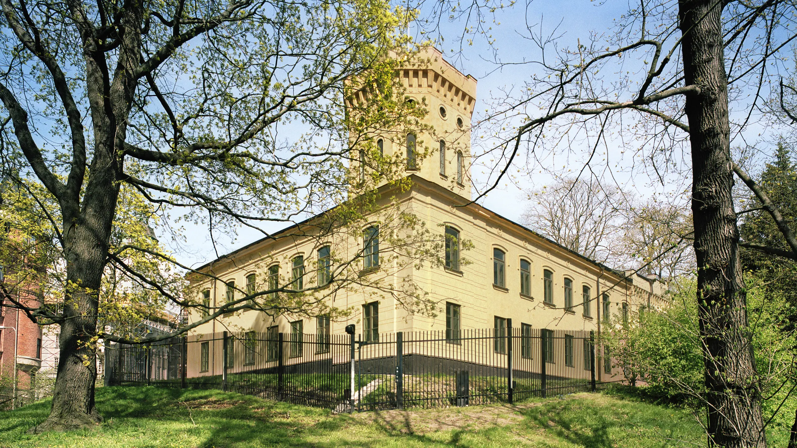 En byggnad i två våningar med fasad i gul puts. I husets hörn finns ett krenelerat torn.