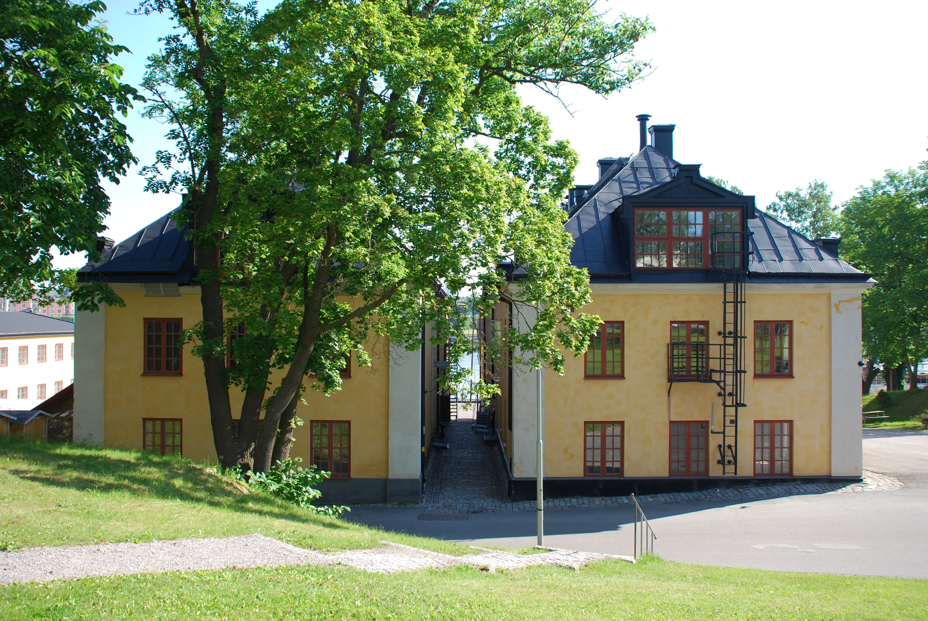 Fundamentshusen på Skeppsholmen. Två likadana gulputsade hus med valmade svarta plåt-tak.