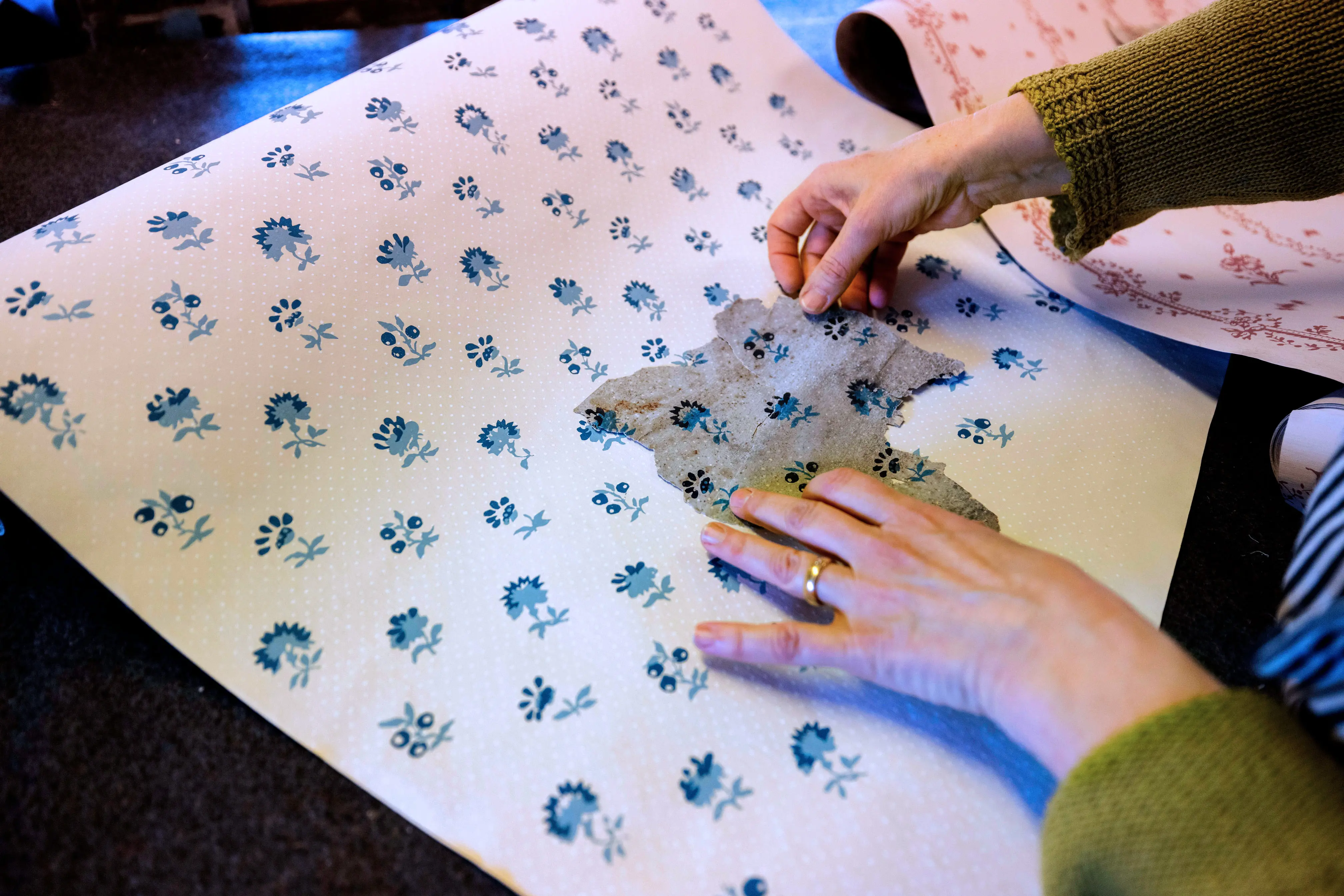 Händer som jämför originaltapetmönster med nytryckt.