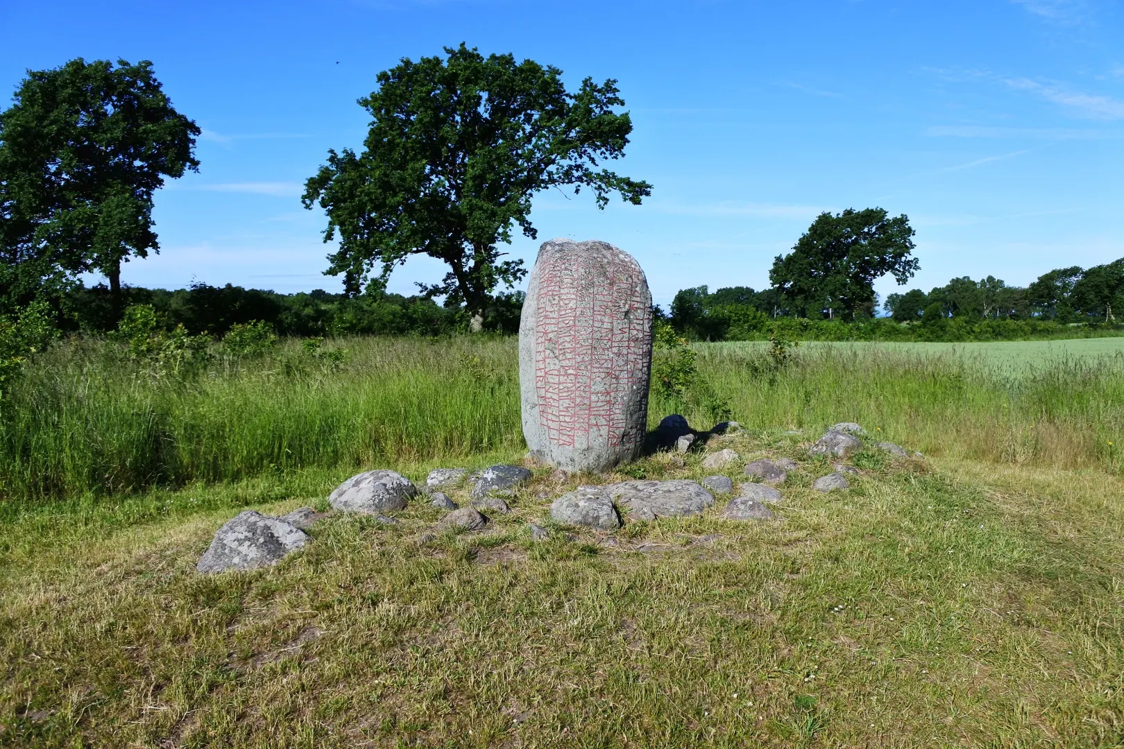 Runstenen Karlevistenen med en åker och några träd i bakgrunden.
