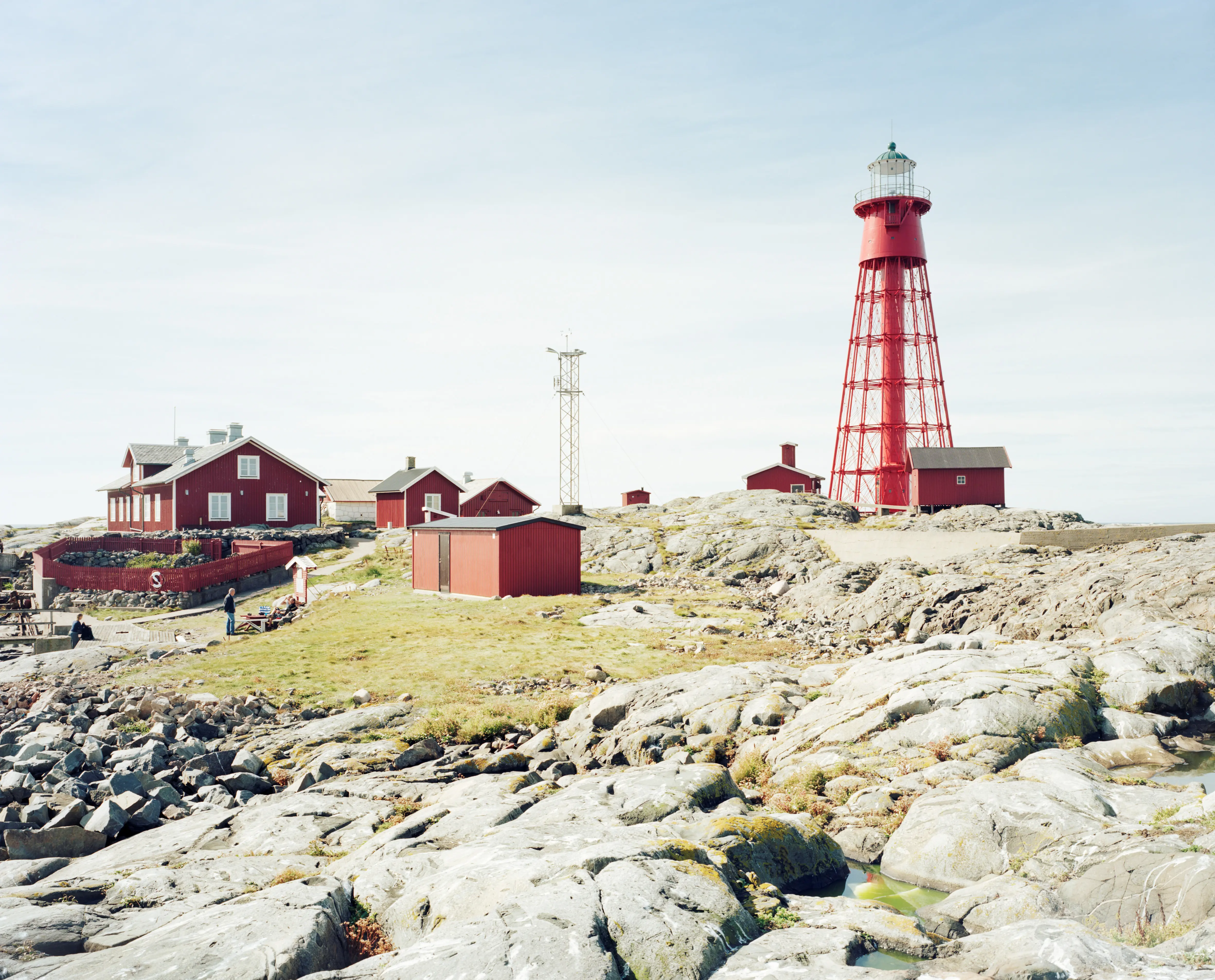 Hamneskärs klippor, röda träbyggnader och fyren Pater Noster sedda från den steniga stranden.
