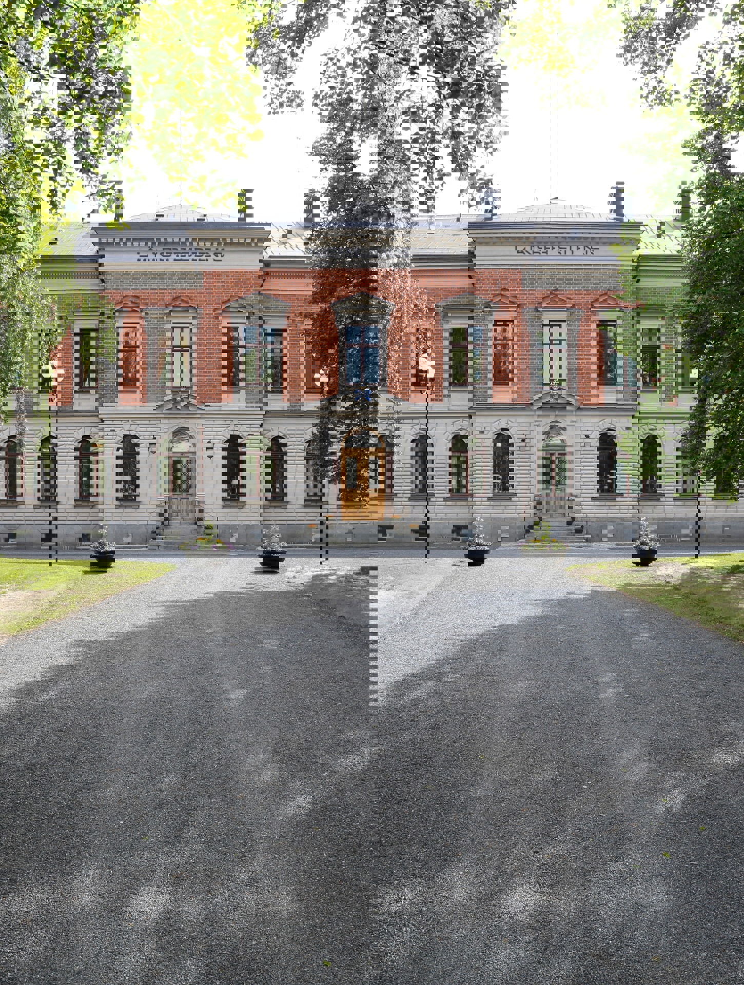 Entréfasaden, Umeå residens. En tvåvåningsbyggnad i tegel och vit puts. Sommar och grönska.
