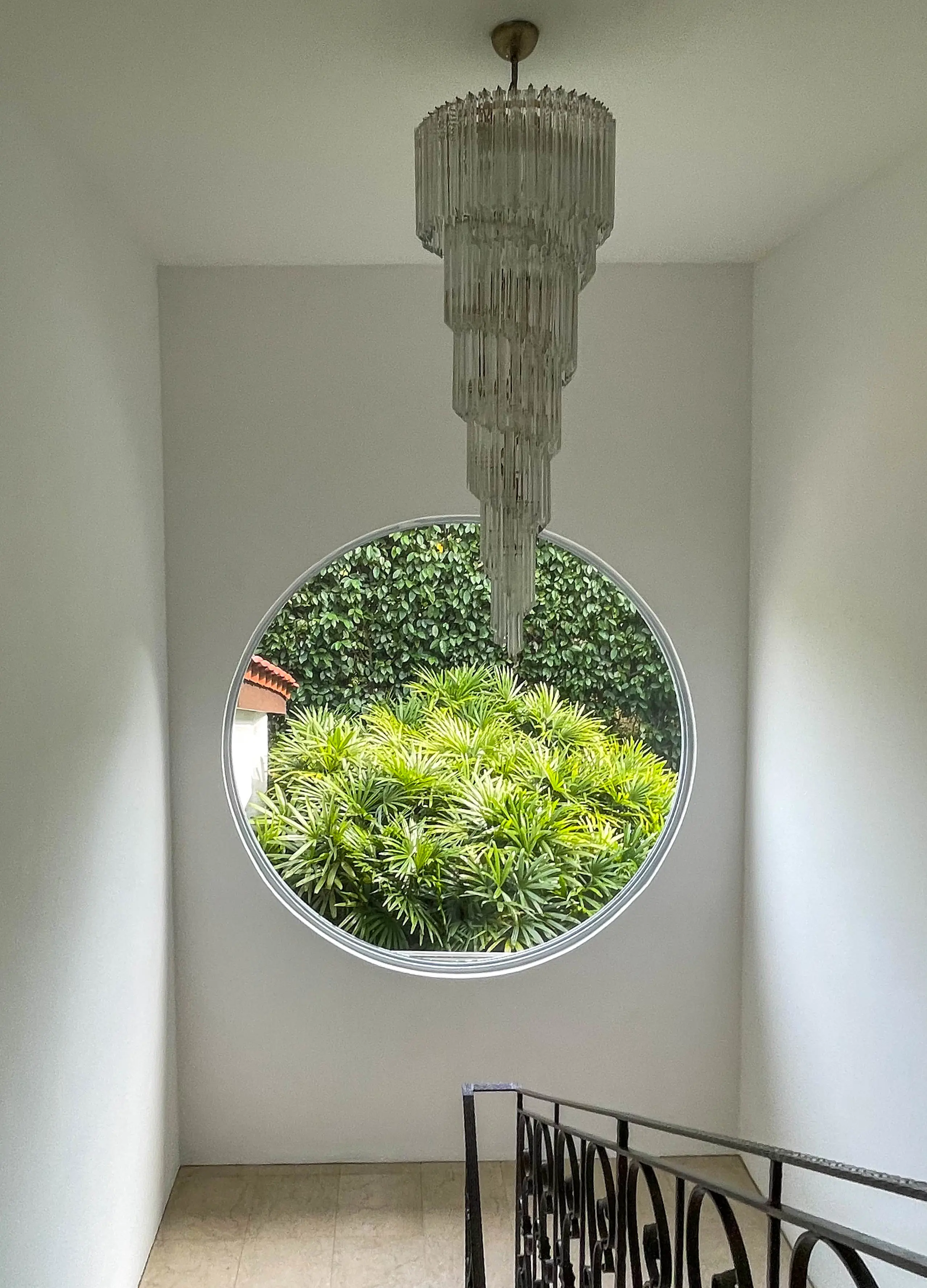 EEtt ljust trapphus med ett stort, rnunt fönster mot grönskande växter. i kaet en långsmal kristallkrona.