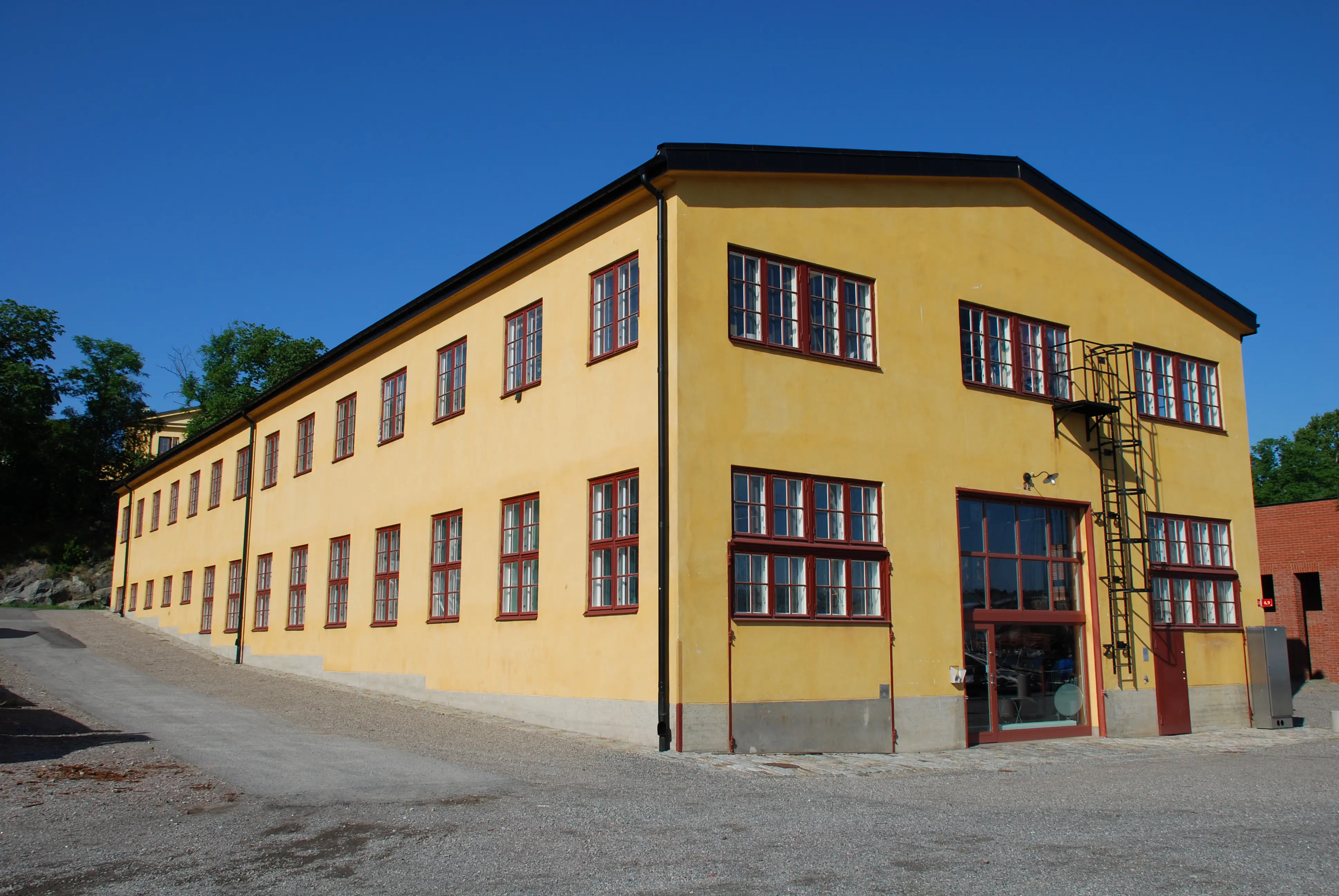 Kanonverkstaden på Skeppsholmen. Gul funkisbyggnad i lätt souterräng.