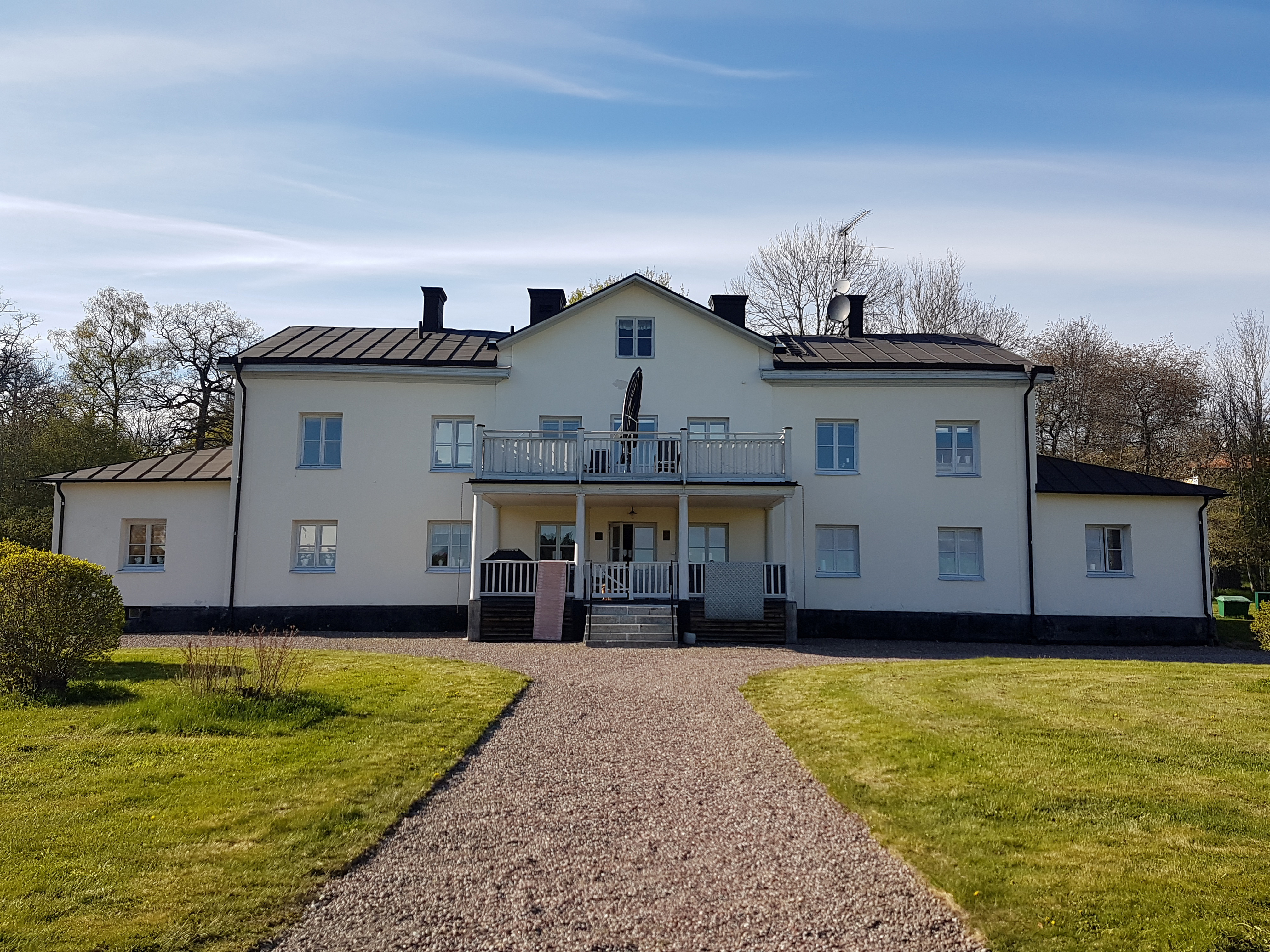 Huvudbyggnaden på Rosersbergs kungsgård. En vitputsad tvåvånings-byggnad med mittgavel och veranda kring entrén.