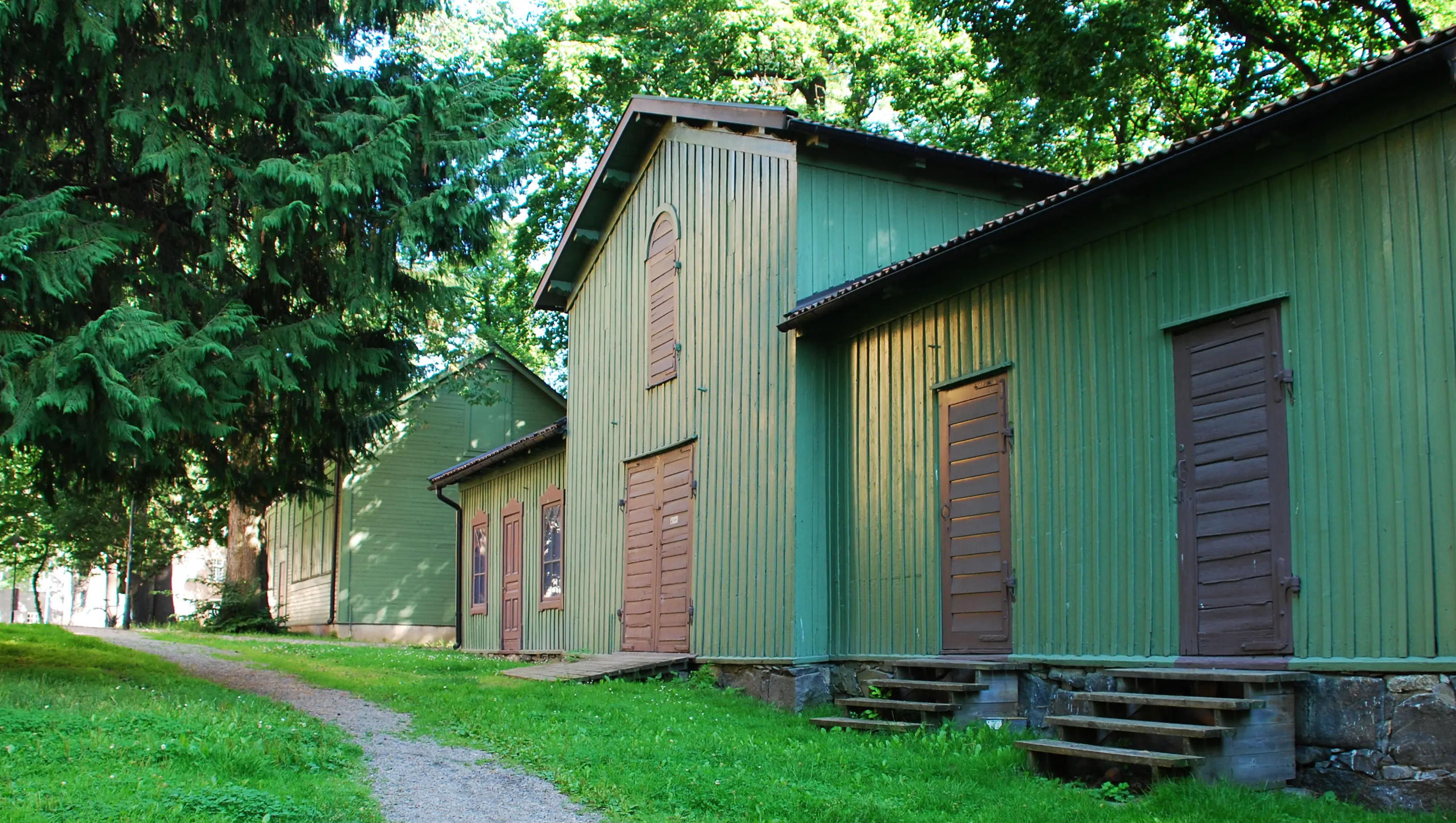 Gamla Skogsinstitutets grönmålade träpaviljonger med svarta dörrar. Sommar och grönska.