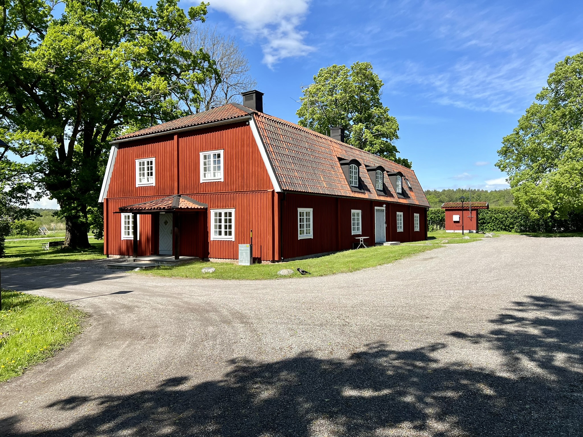 Tingshuset vid Svartsjö slott. En röd tvåvåningsbyggnad med tegeltak och tak-kupor. Sommar och grönska.