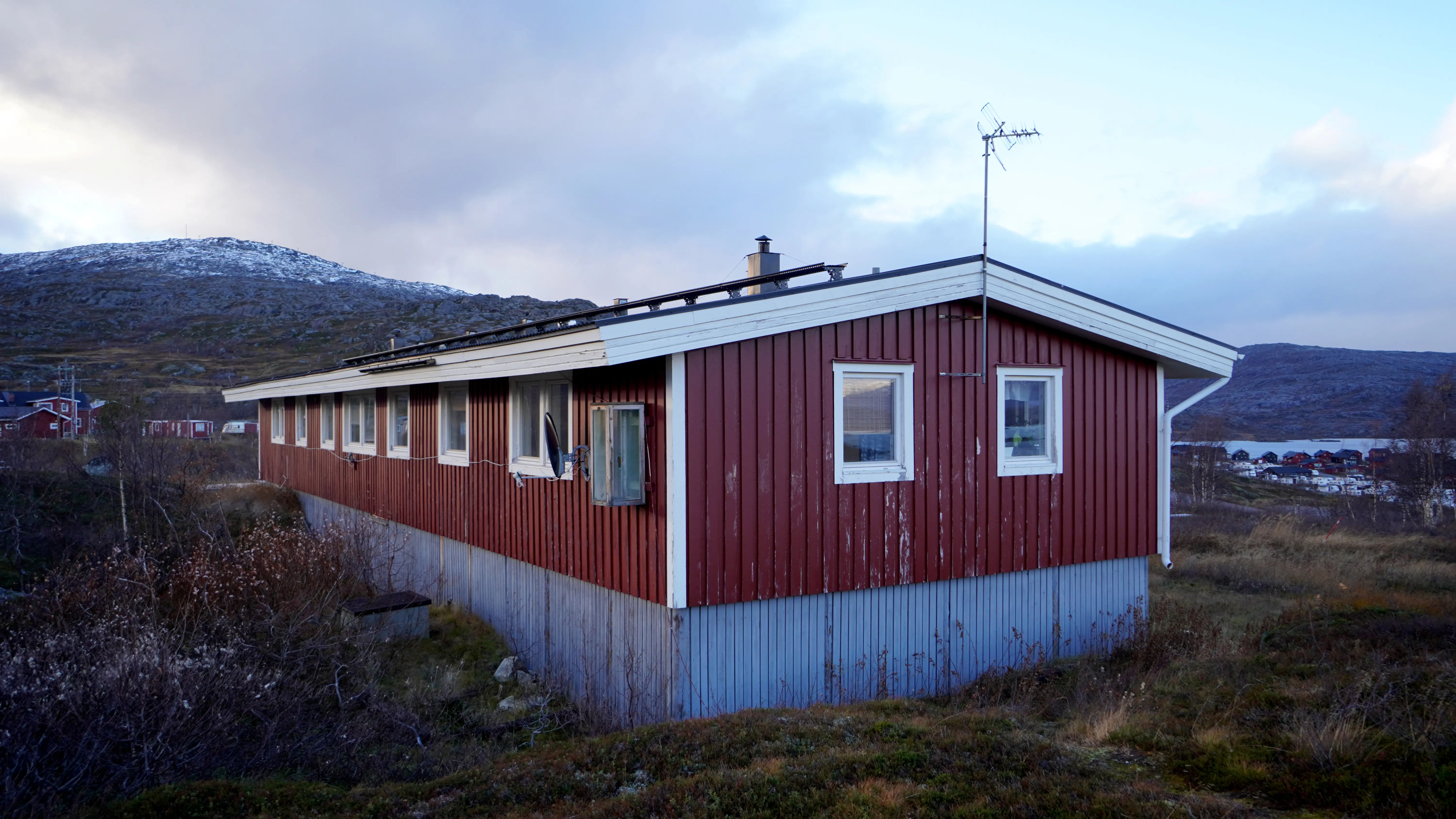 Ett rött hus med vita knutar i ett fjällandskap med blåaktigt kvällsljus.