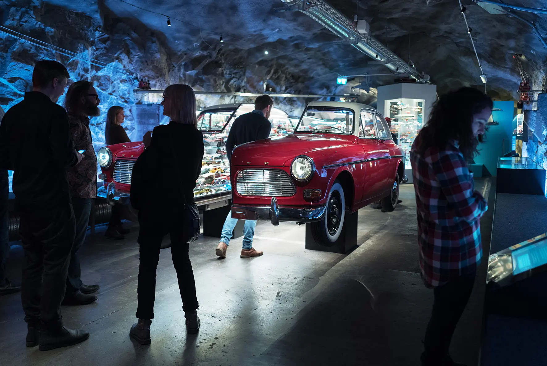 En delad röd Volvo Amazon och museibesökare som tittar på utställningen inne i bergrummet.