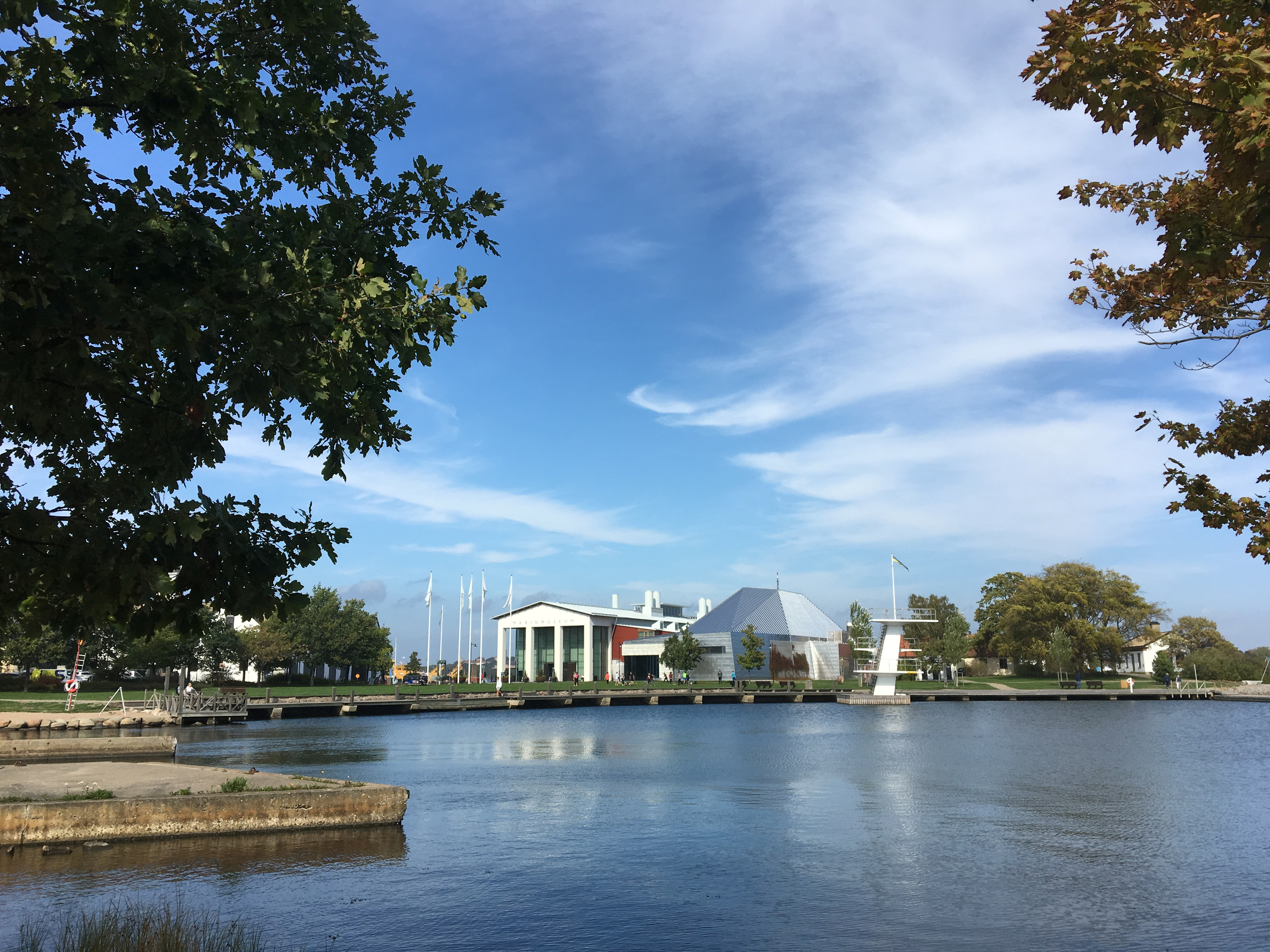 Marinmuseum och ubåtshallen i Karlskrona, sedda över vattnet. Ubåtshallen är välvd som en båt med kölen i vädret. Marinmuseum är stramt klassicistisk.