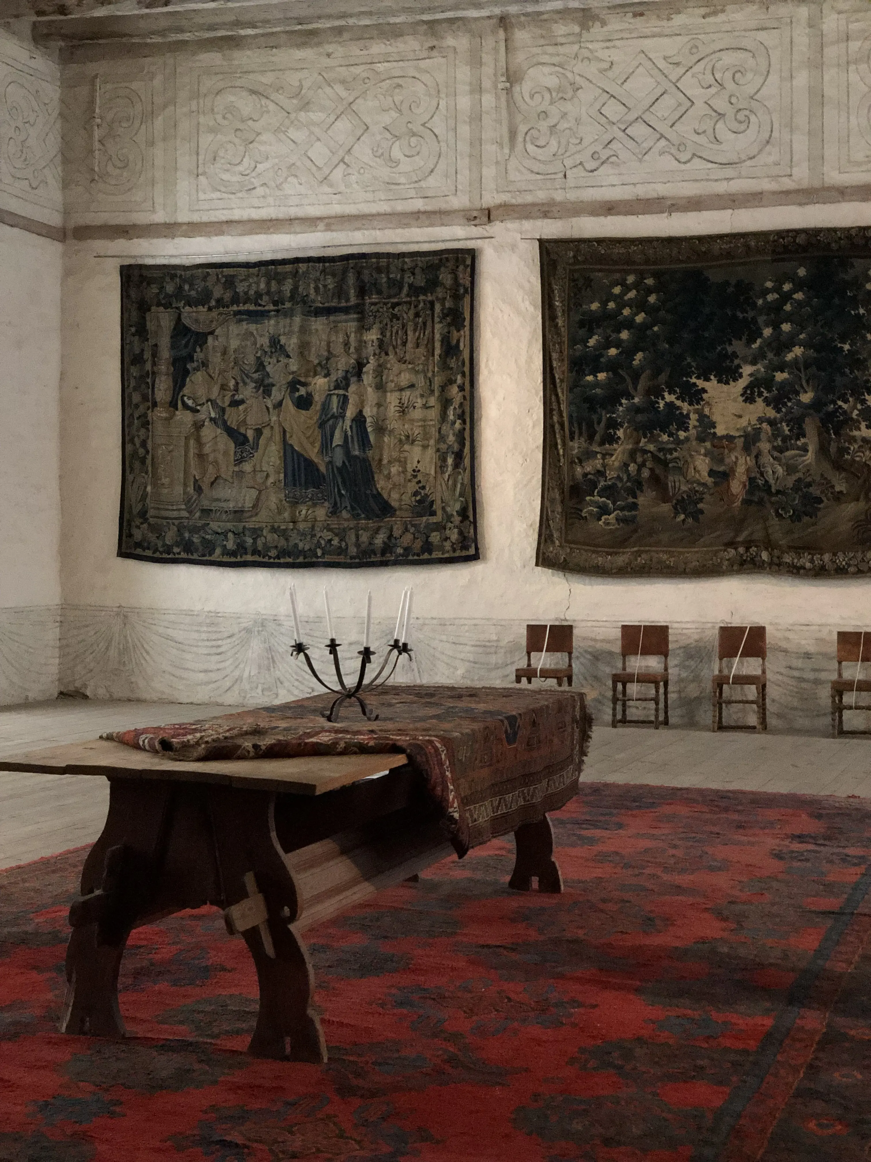 Interiör, Vadstena slott. Sal med väggmålningar och gobelänger. Ett träbord står på en röd matta med svart mönster.