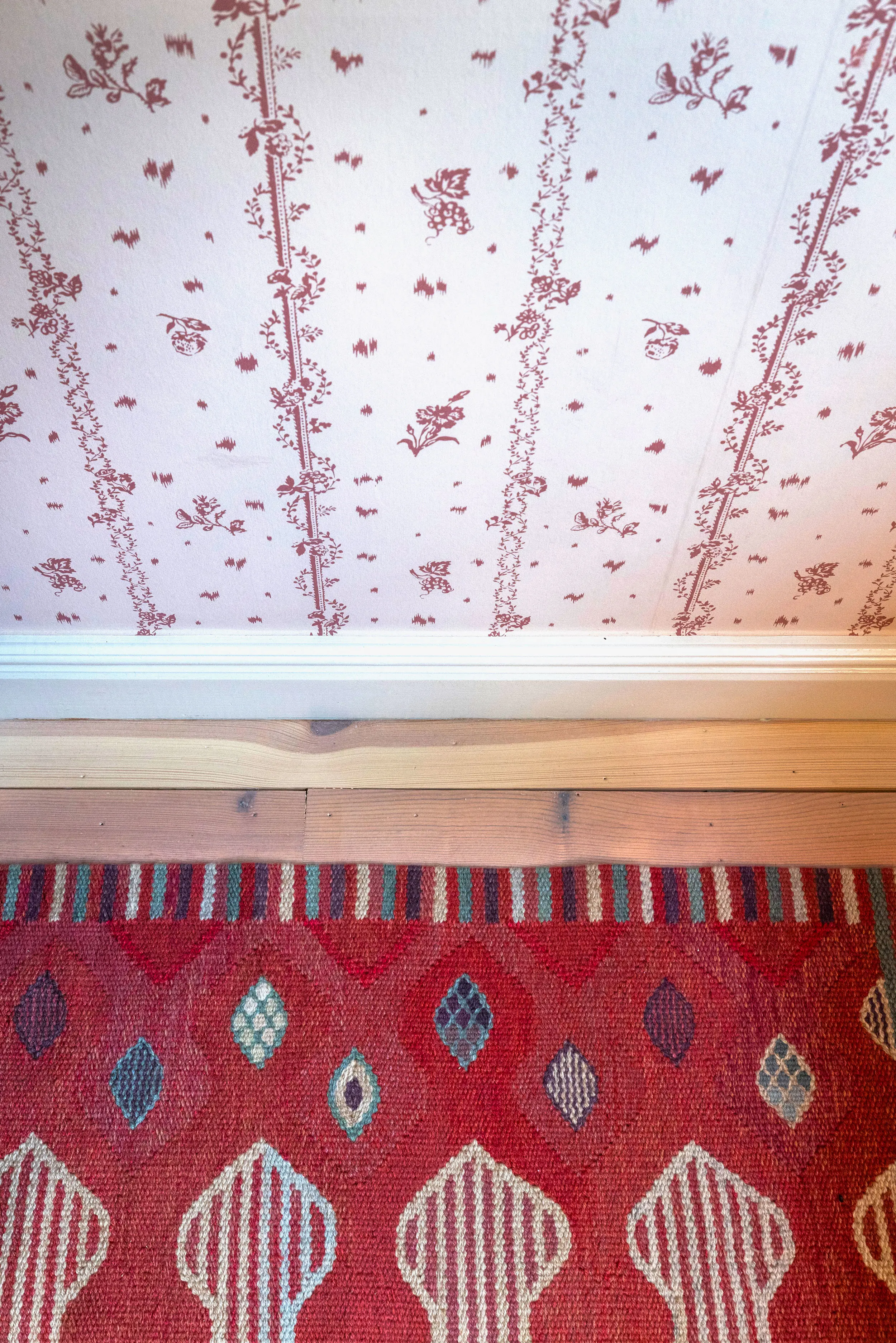 Tapet med röda blomsterslingor och röd matta med rombformer.