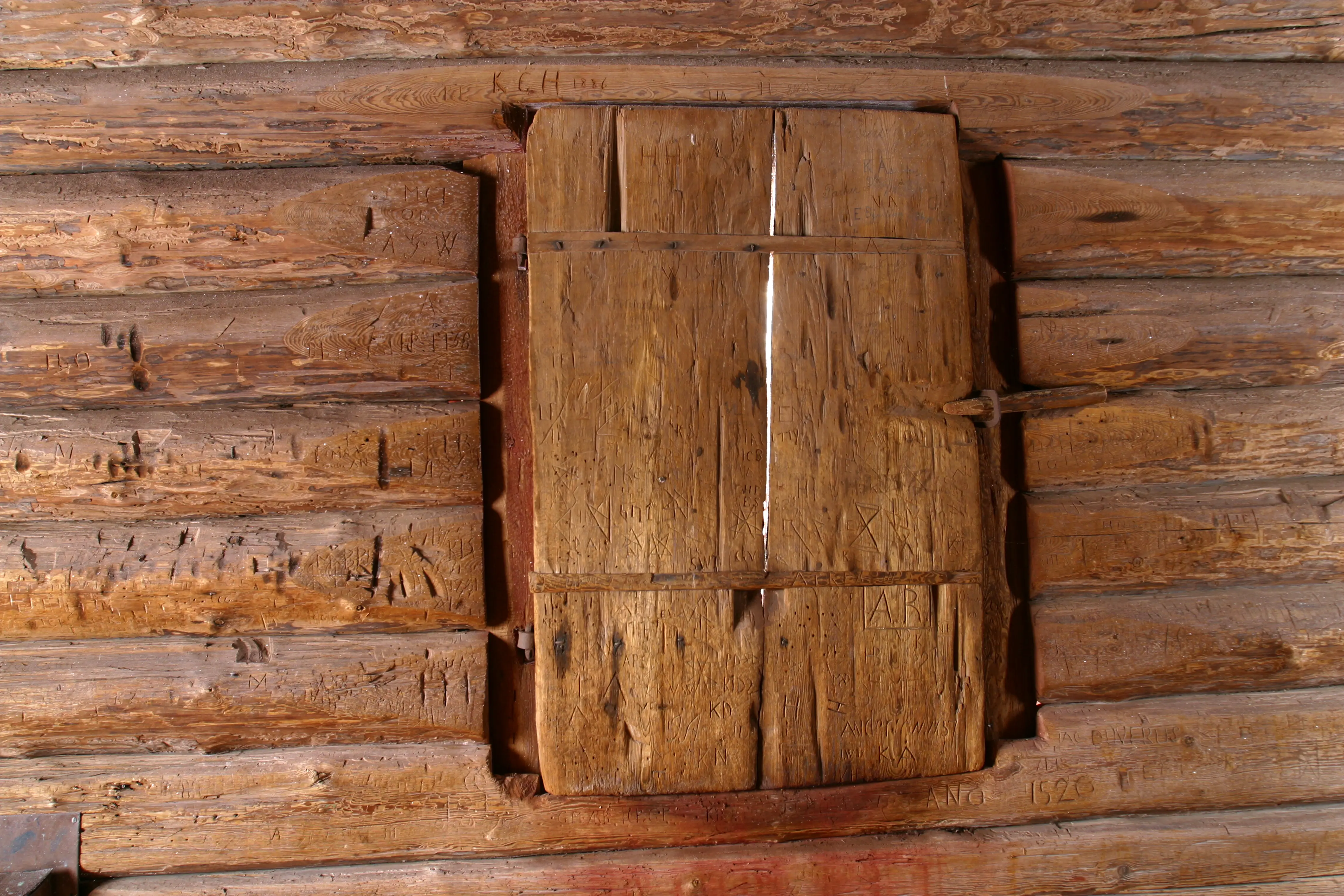 Rankhyttan. Grov timmerinredning. Träluckor täcker en fönsteröppning.