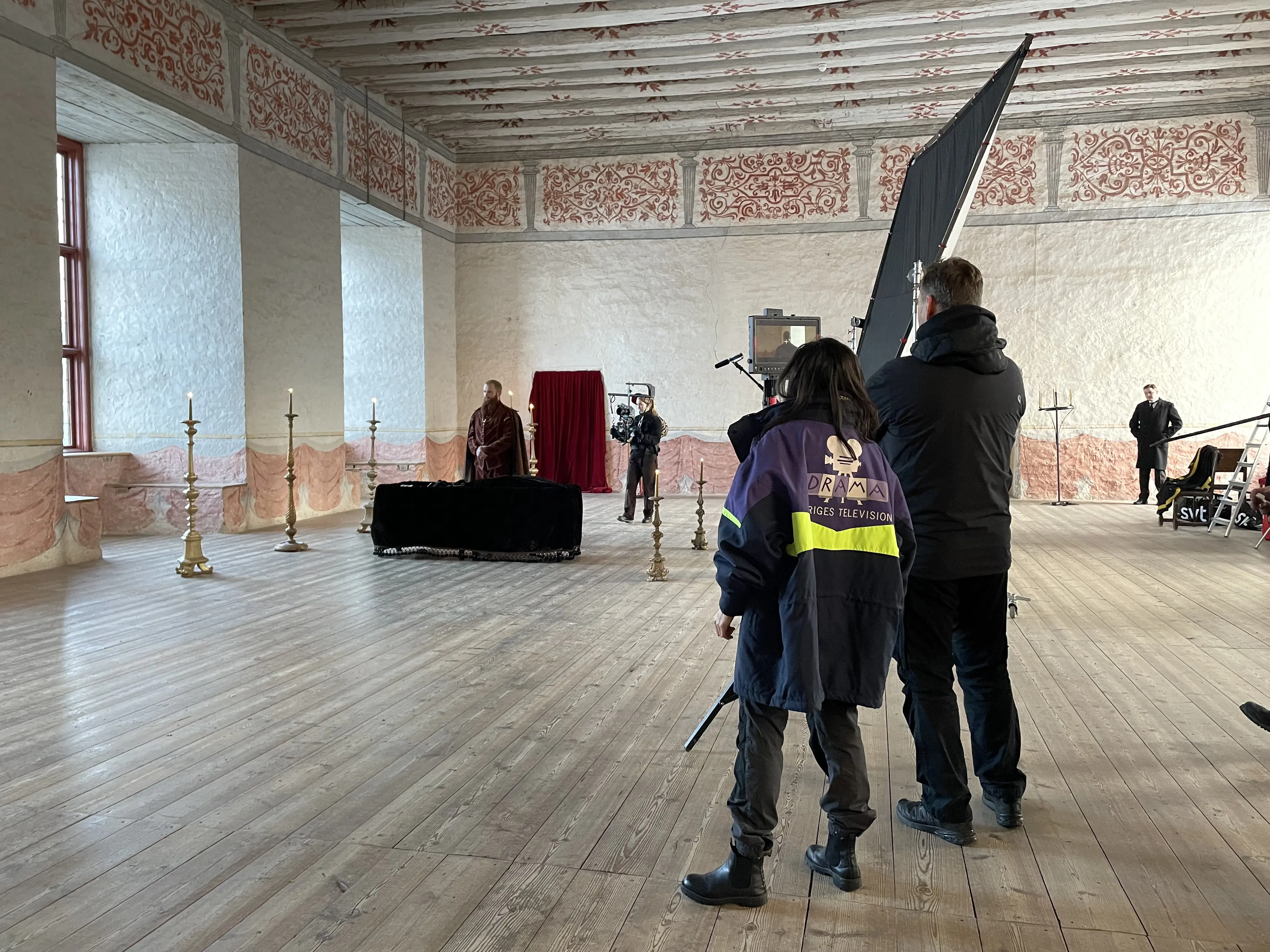 Filminspelning i en slotts-sal med målade väggar. En historisk scen blir filmad.