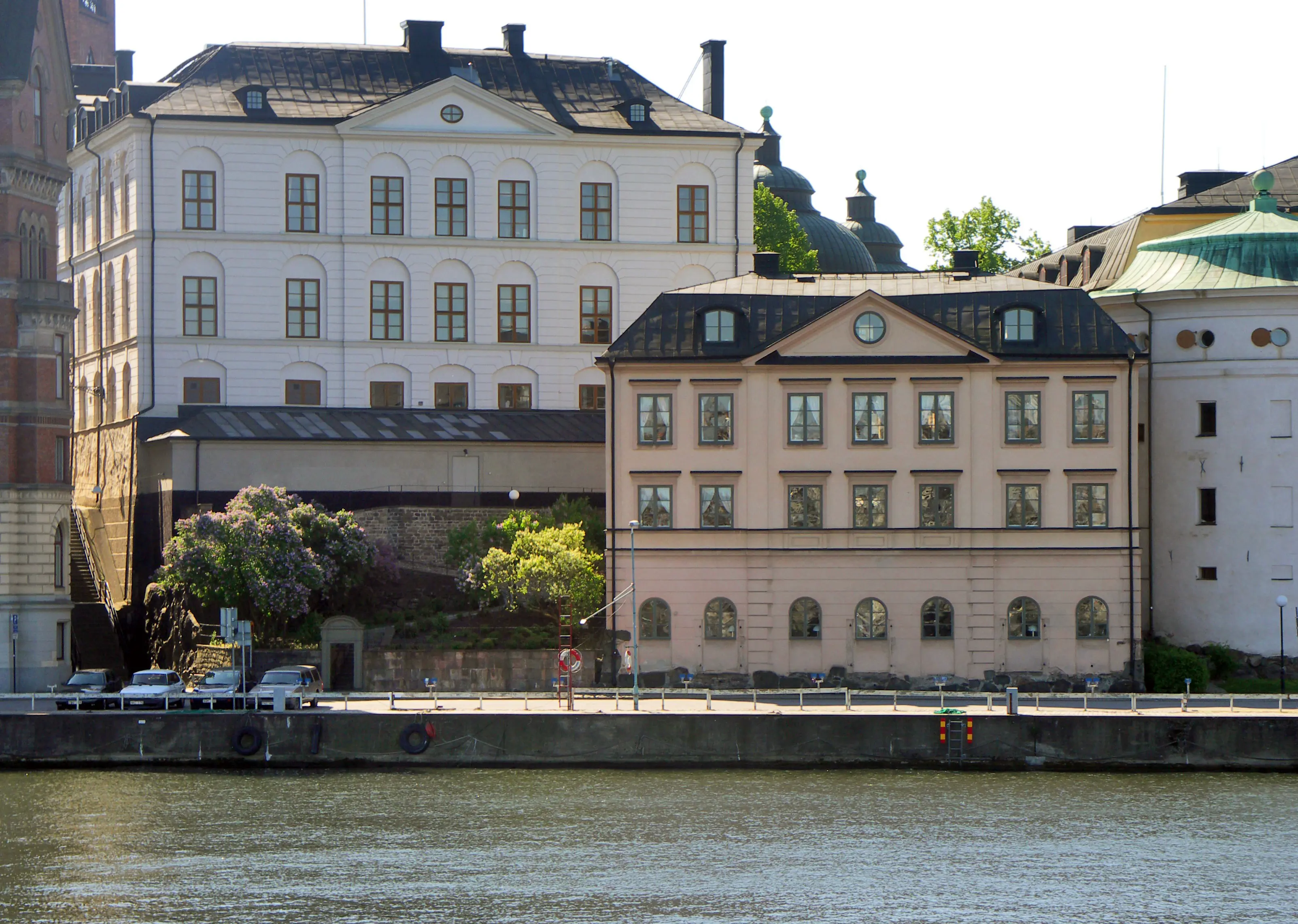 Överkommissariens hus. Ett gräddvitt hus i suterräng. Fasaden mot vattnet har tre våningar. Sommar och grönska.