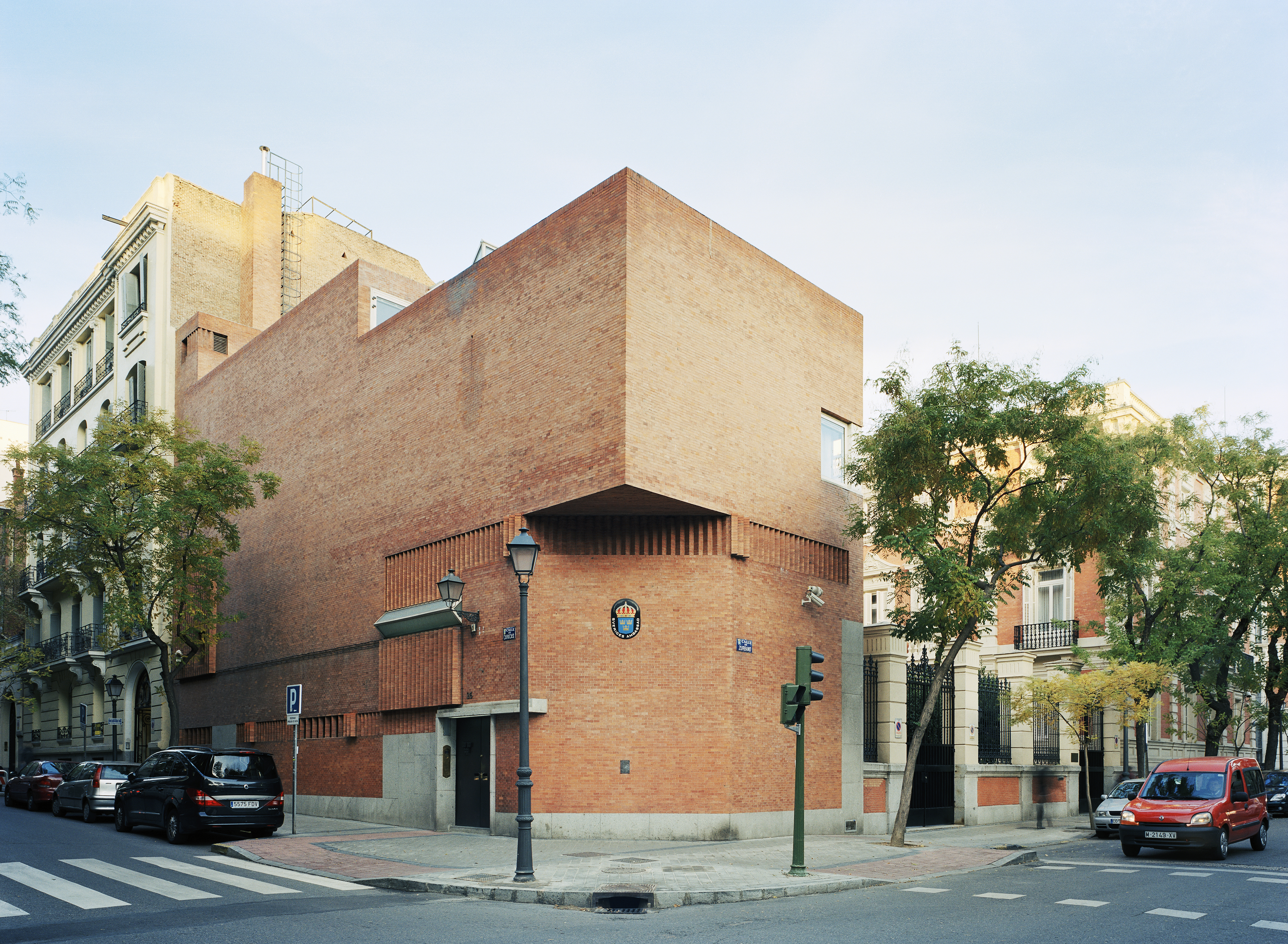Ambassaden i Madrid. En modernistisk, slät tegelbyggnad utan fönster mot gatan. I bakgrunden skymtar den äldre, utsmyckade byggnaden.