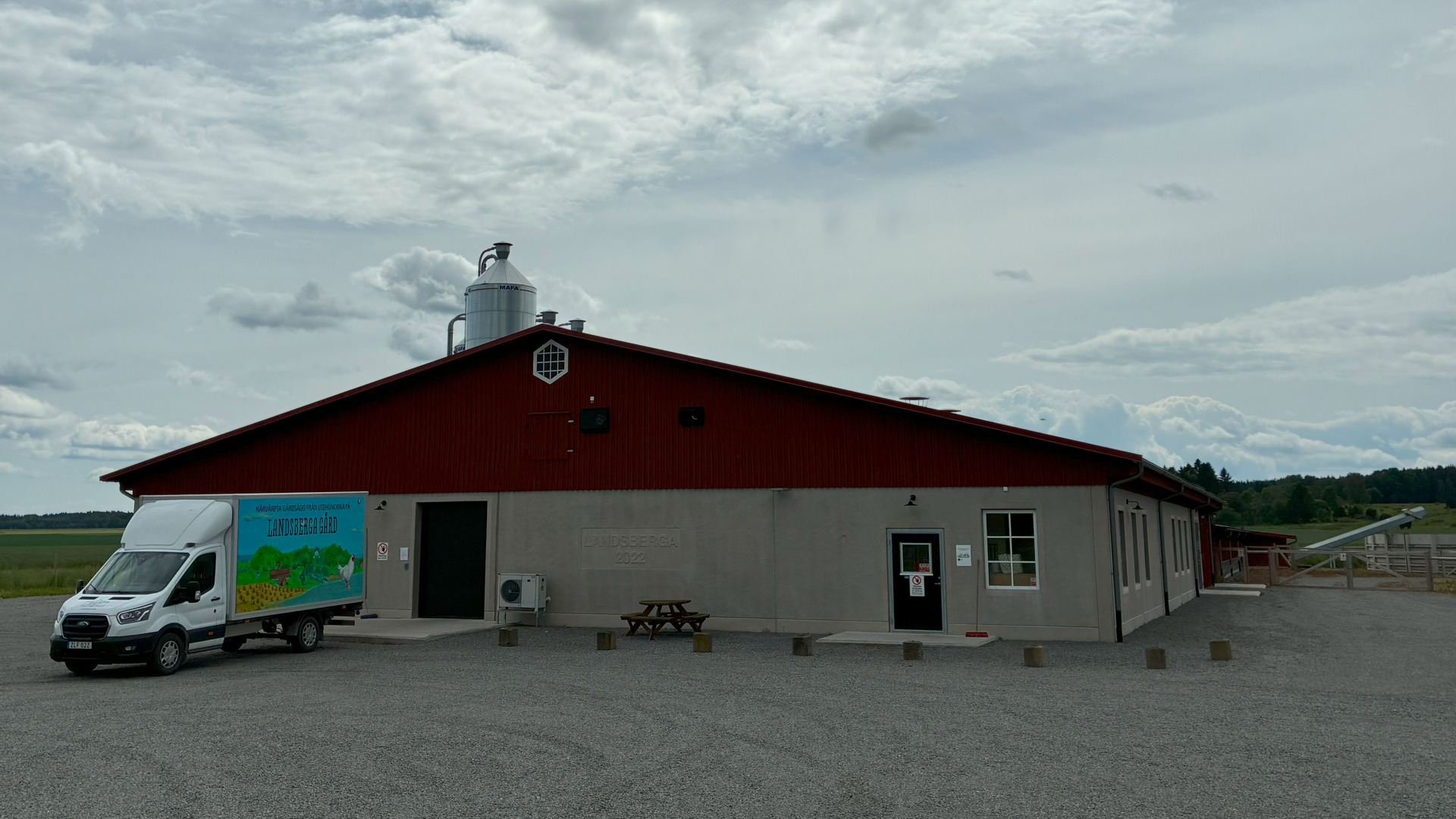 Landsberga. Grå betongbyggnad med rött tak. På grusplanen framför huset står en liten lastbil för äggleverans.