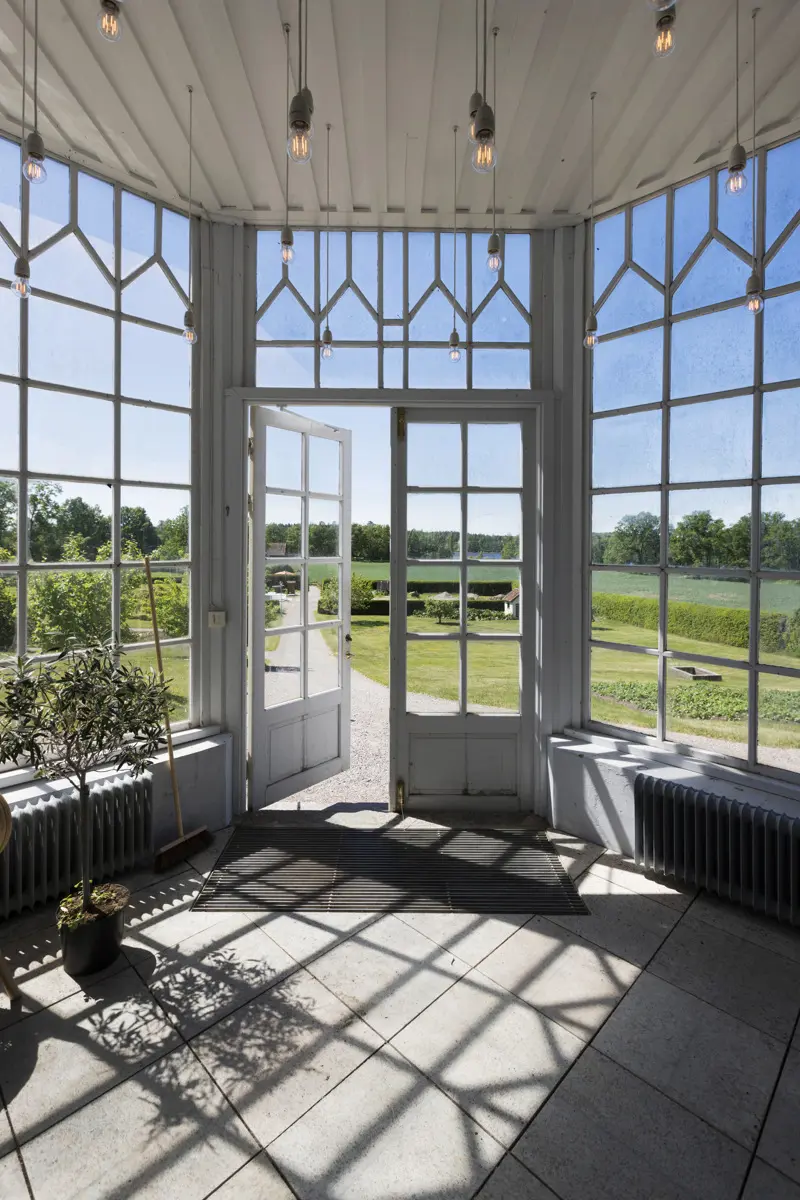 Växthus med fönsterfris och utsikt över solig åkermark.