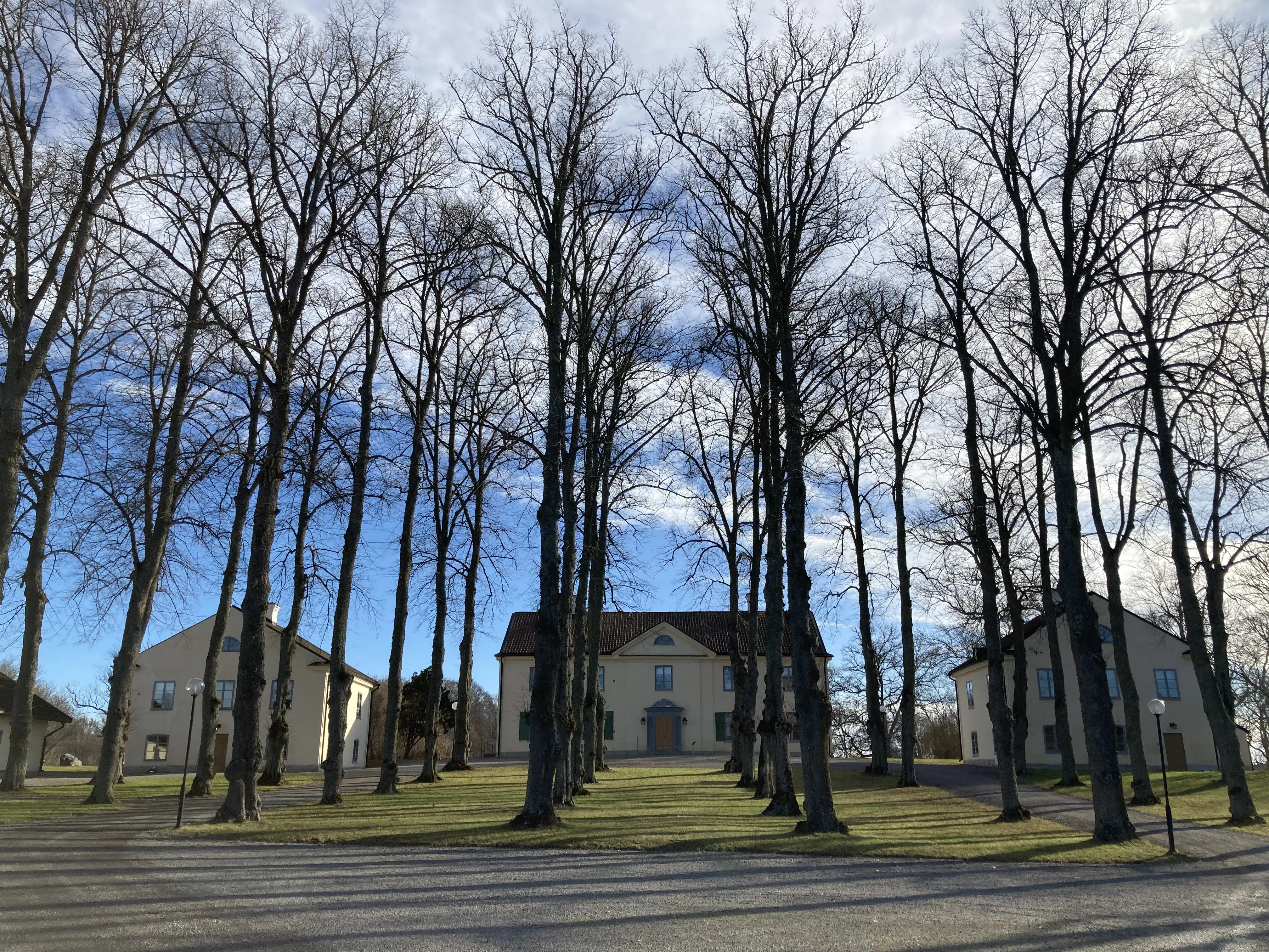 Biskops Arnö. Huvudbyggnad och flyglar sedda genom alléer. Tidig vår.