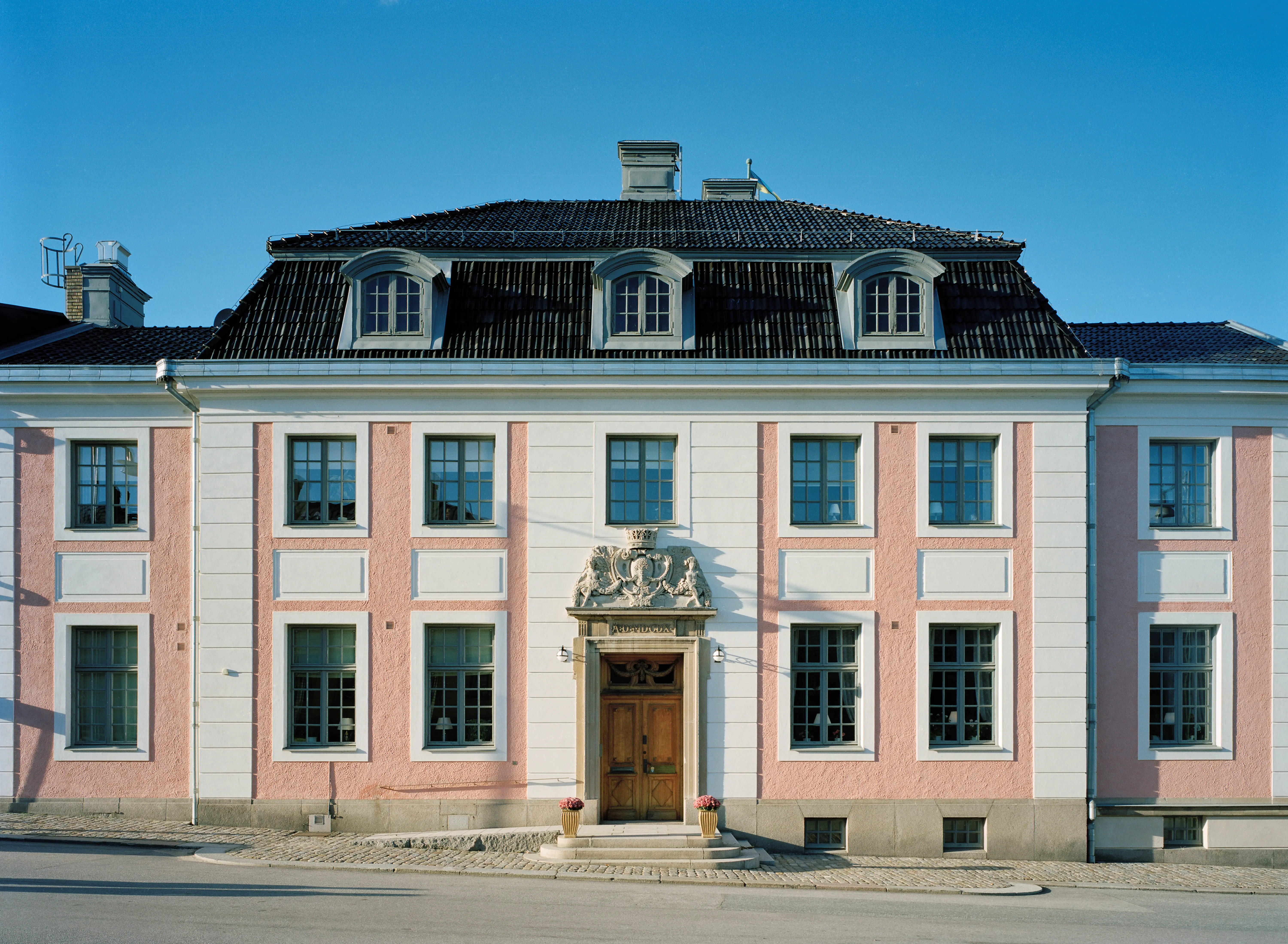 Residenset i Karlskrona. En rosaputsad byggnad med vita pilastrar. Taket är brutet med takkupor. Entrén omges av en stenportal krönt med Blekinges vapen.