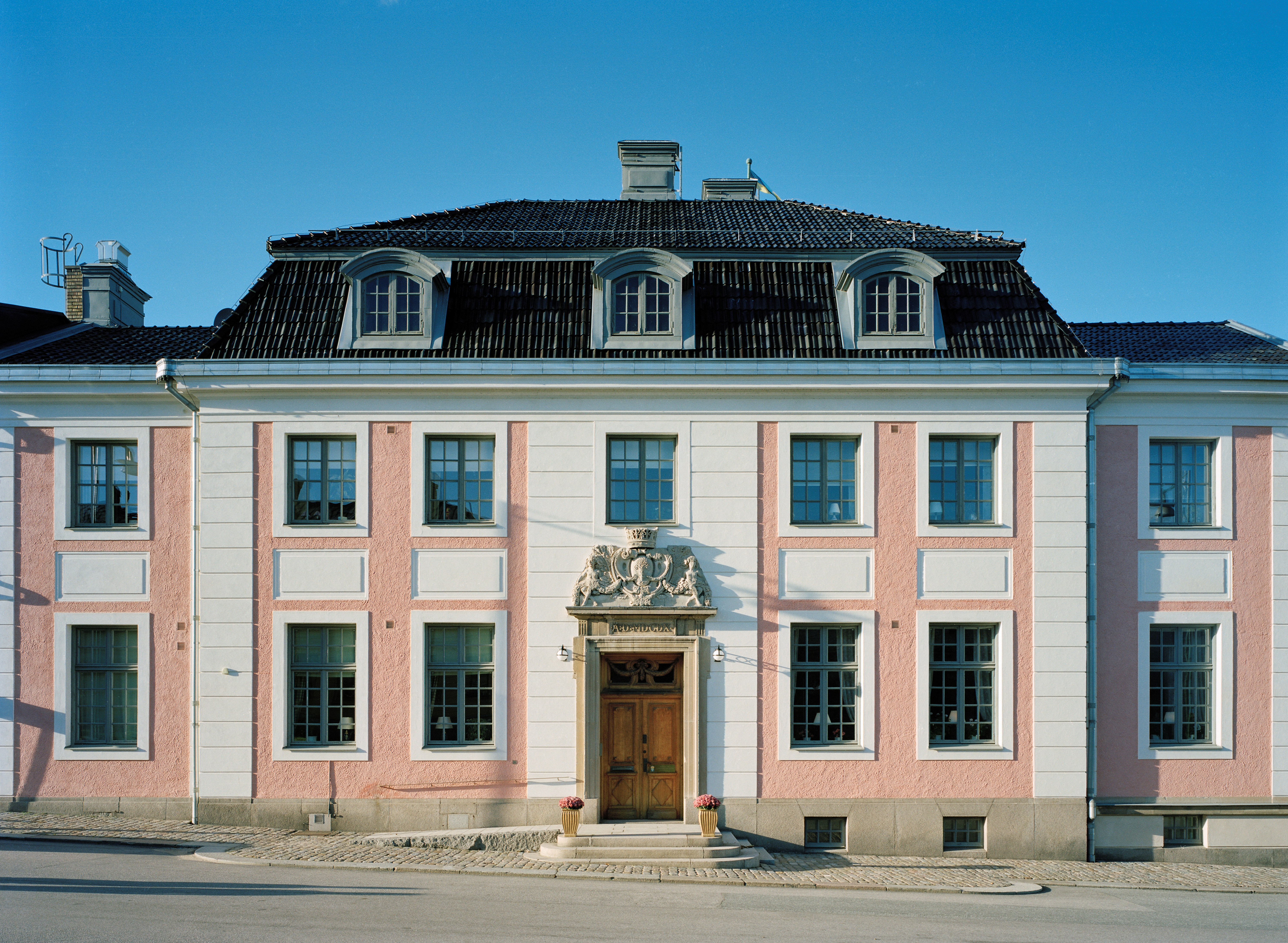 Residenset i Karlskrona. En rosaputsad byggnad med vita pilastrar. Taket är brutet med takkupor. Entrén omges av en stenportal krönt med Blekinges vapen.