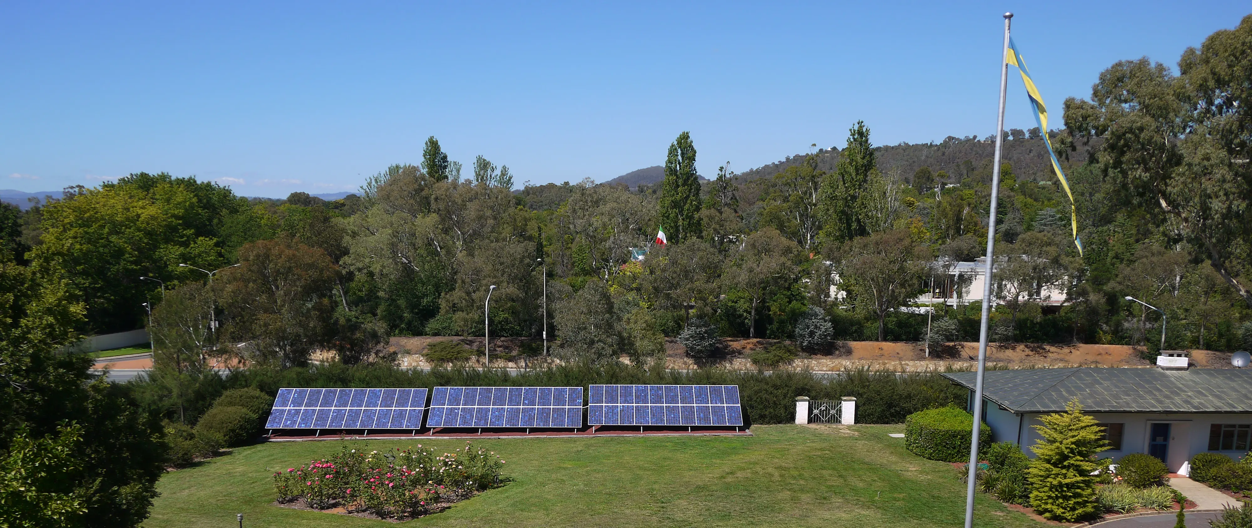 Canberra, ambassadens trädgård med de stora solpanelerna. Vy mot kullar och berg med tät växtlighet.