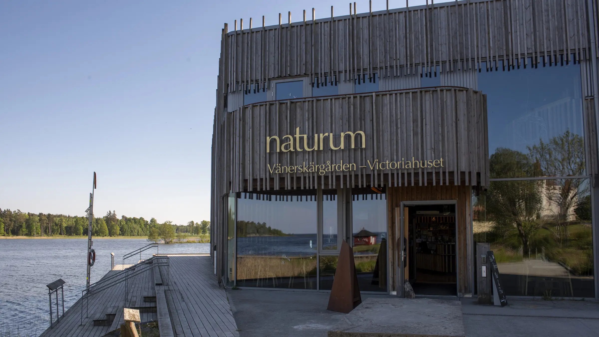 Entrén till Naturum Vänerskärgården. Stora glaspartier ramas in av smal, stående obehandlad träpanel.